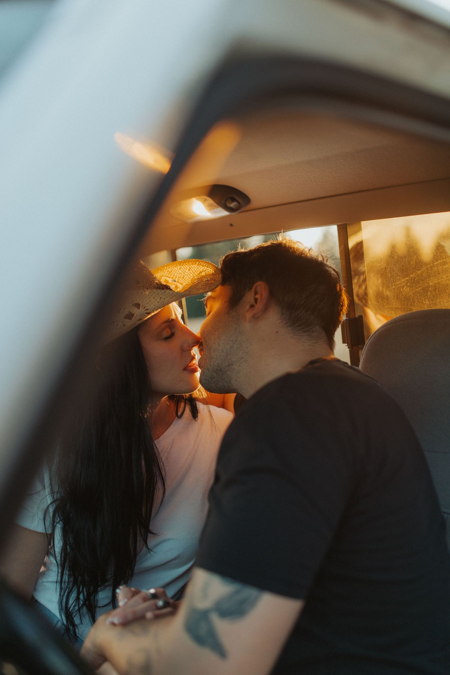 A tattooed couple shares a tender kiss inside a vintage van at golden hour.