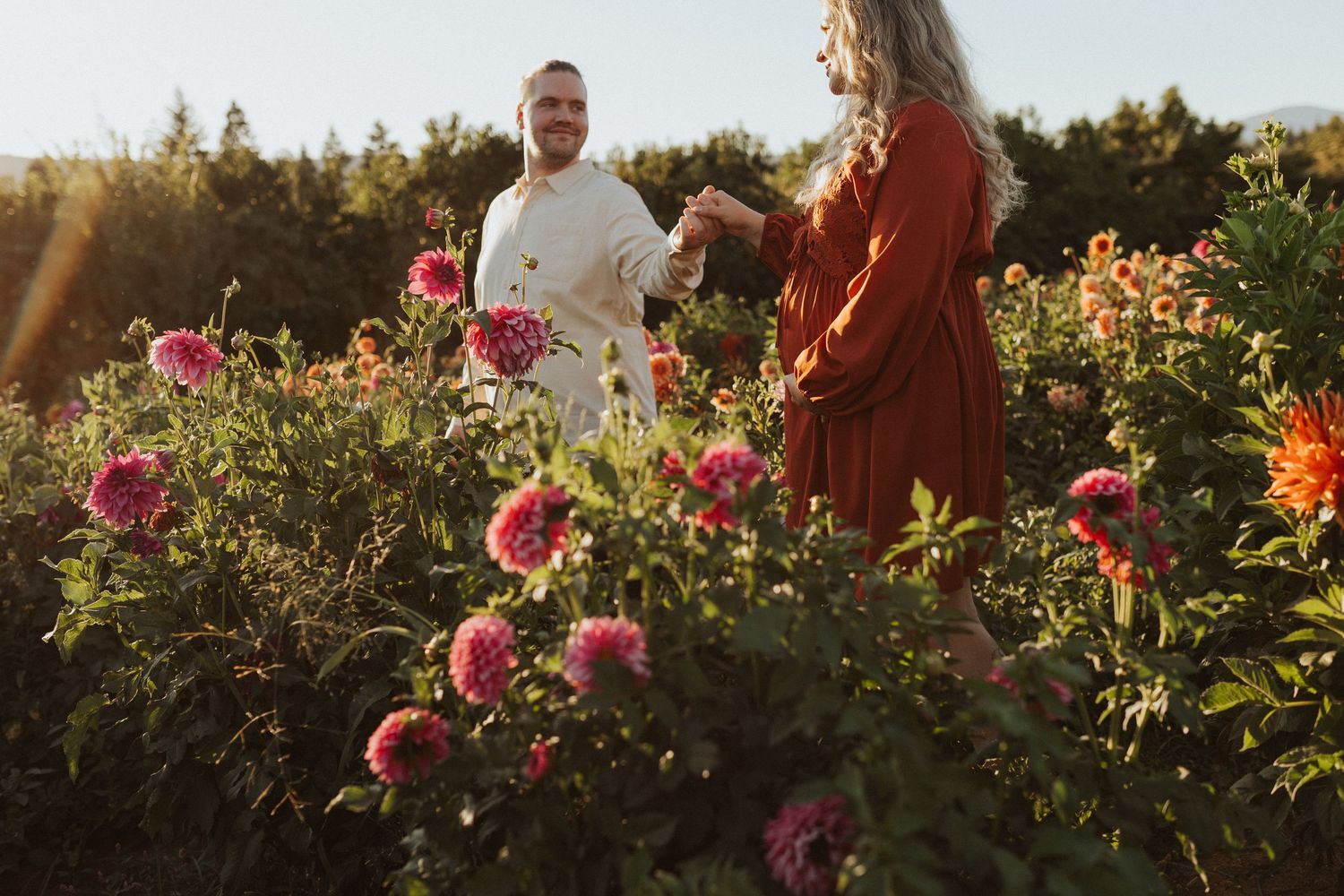 Couple holding hands in a vibrant dahlia flower field at golden hour.