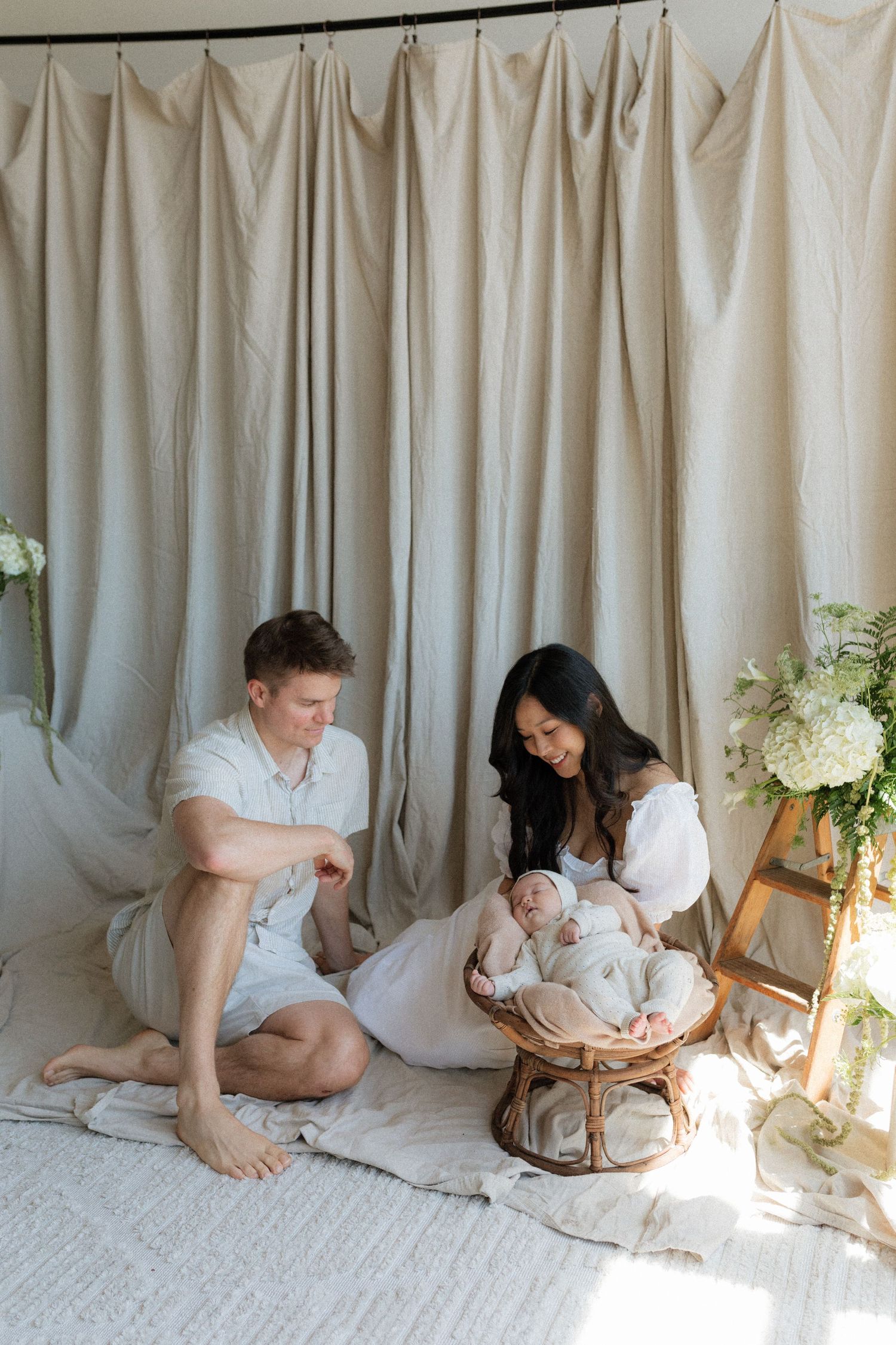 New parents sit on the floor smiling at their newborn baby resting in a wicker basket.