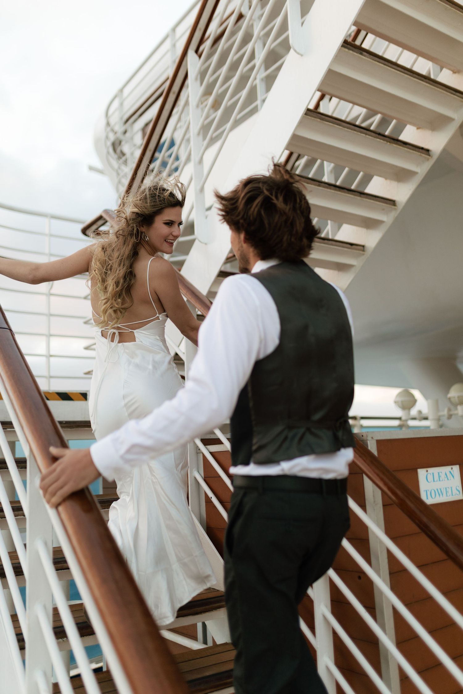 Bride and groom climbing outdoor stairs on a cruise ship deck on their wedding day.