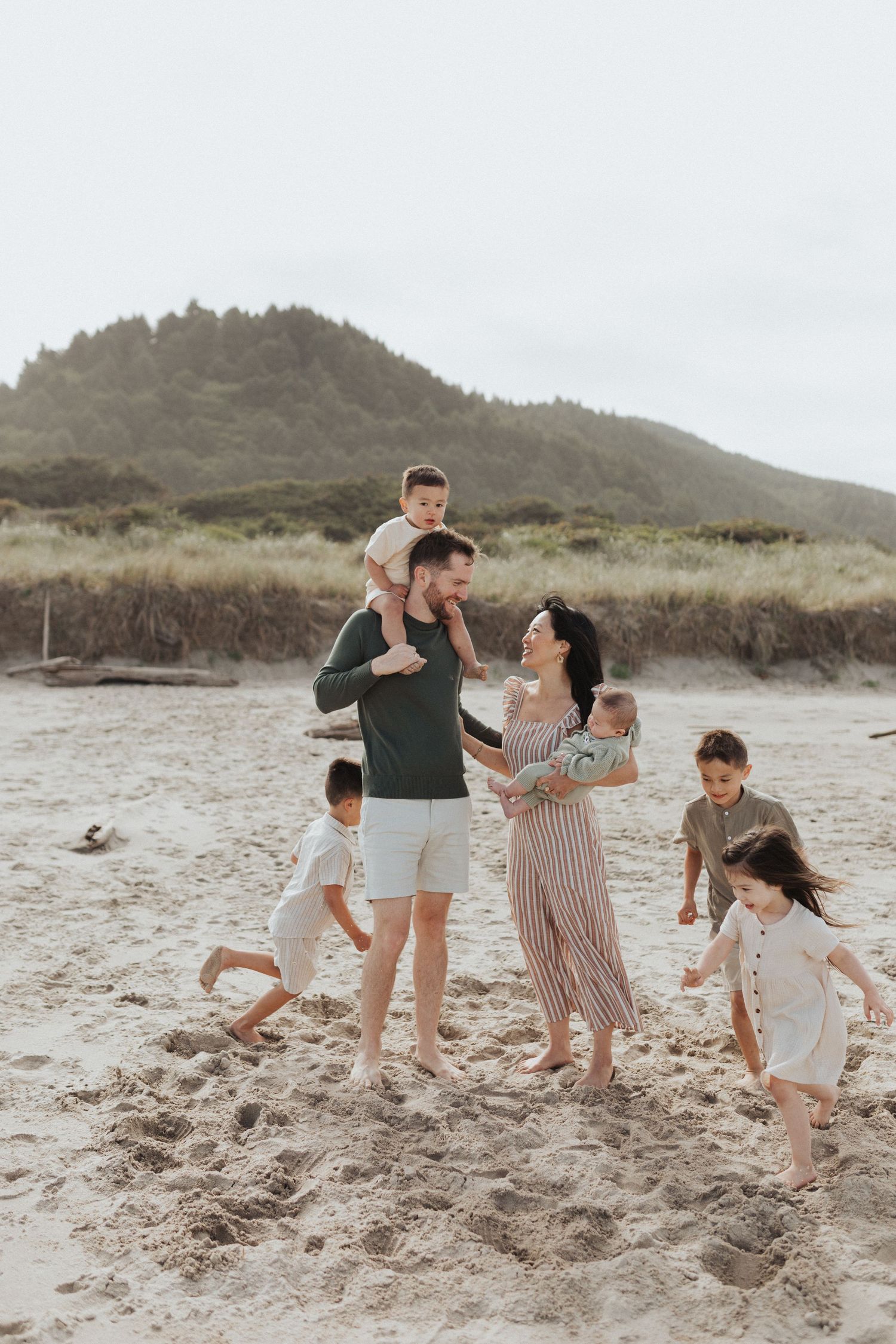 Lively family of seven with five kids playing and laughing together on a sandy beach.