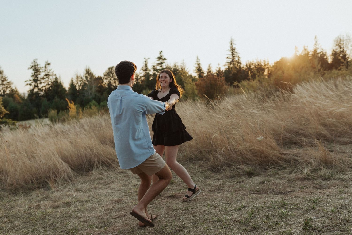 Young couple playfully spinning together in a golden grass field at sunset.