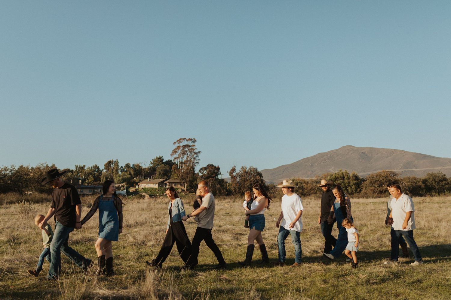 Large family group walking in a line across a golden field with mountain in background.