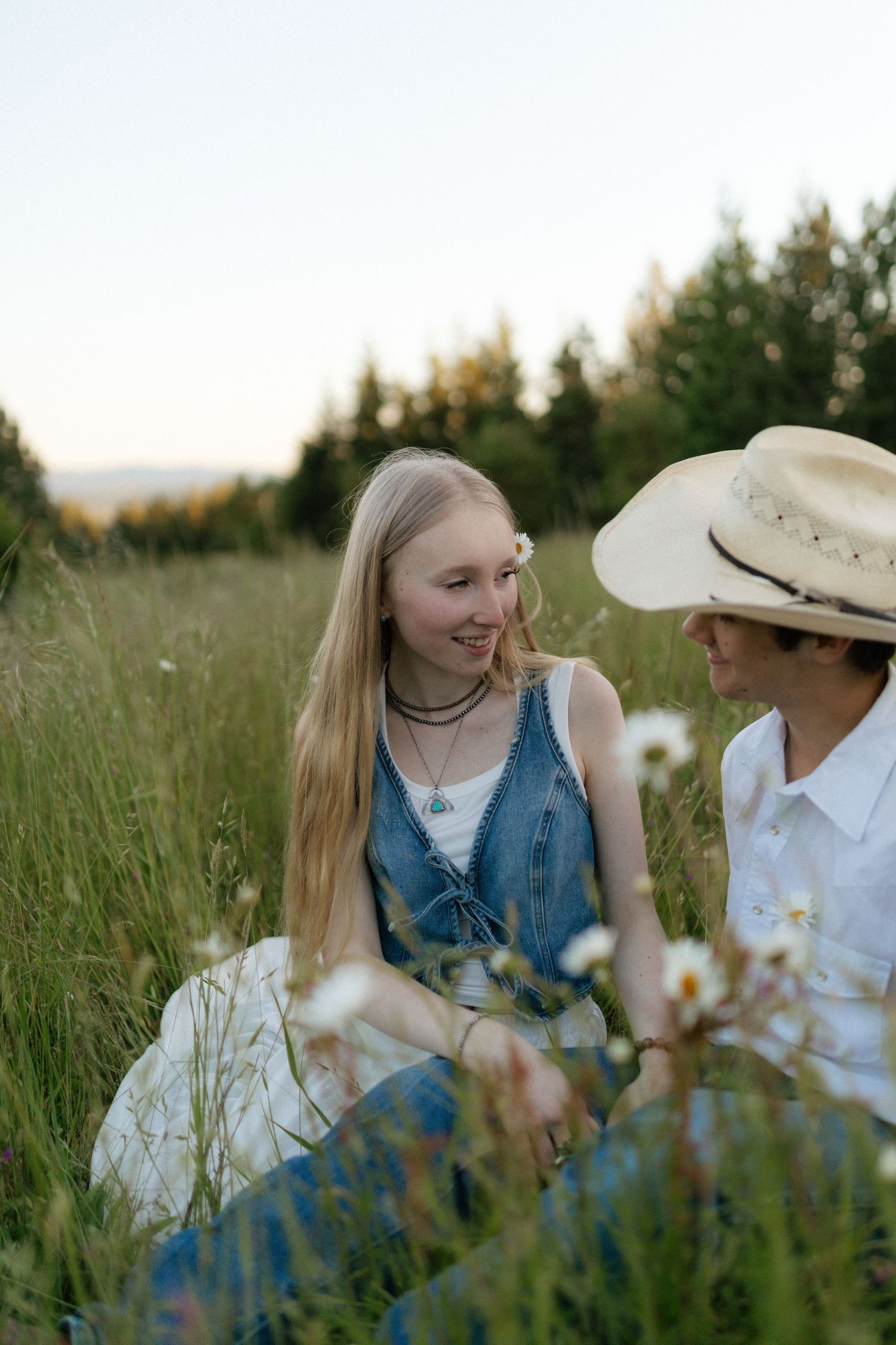 Couple sitting in a wildflower field at sunset, smiling and gazing at each other romantically.