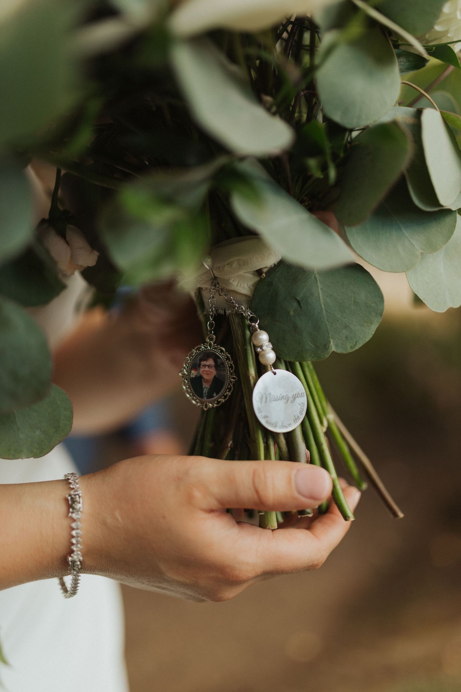 Close-up of wedding bouquet handle adorned with a memorial photo charm and pearl pendant reading missing you.