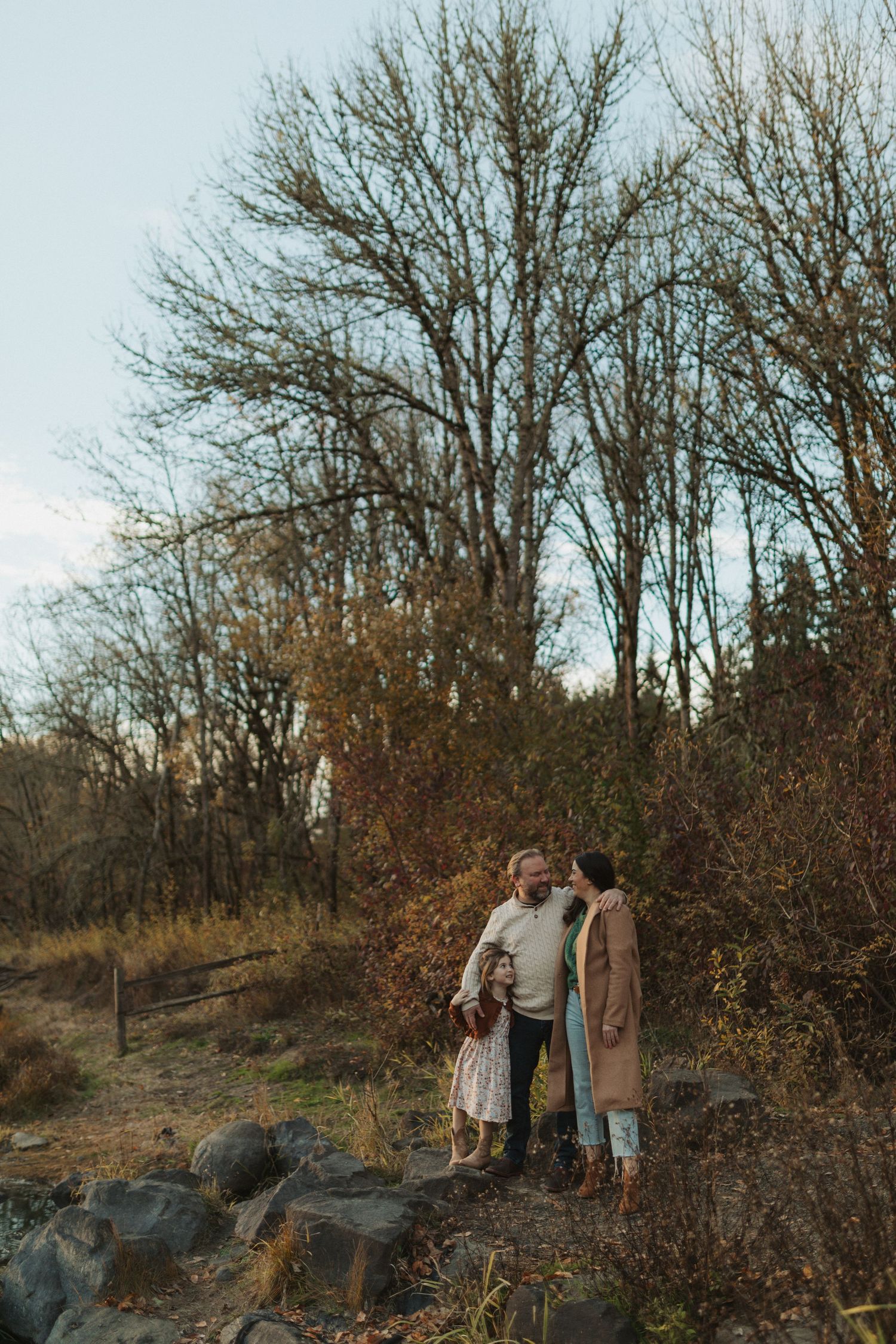 A couple shares a tender moment among bare autumn trees during a fall family photo session outdoors.
