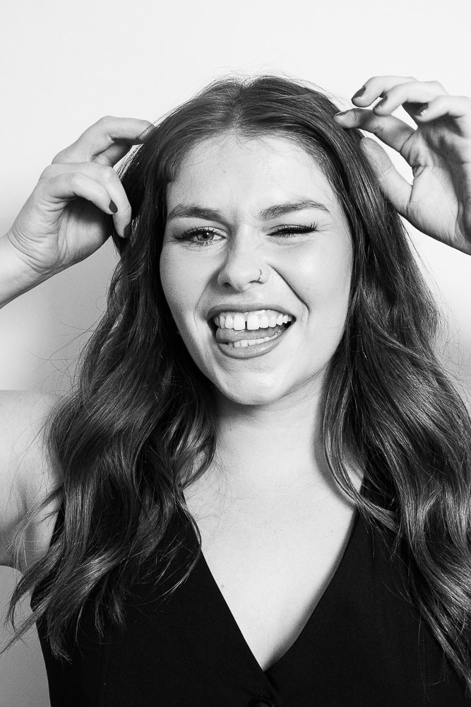 Black and white portrait of a laughing young woman with wavy hair, winking and holding her hair up playfully.