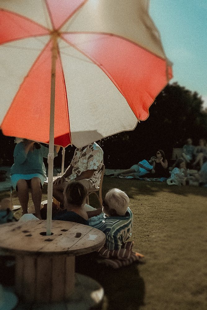 People relaxing outdoors under a red and white striped beach umbrella on a sunny day.