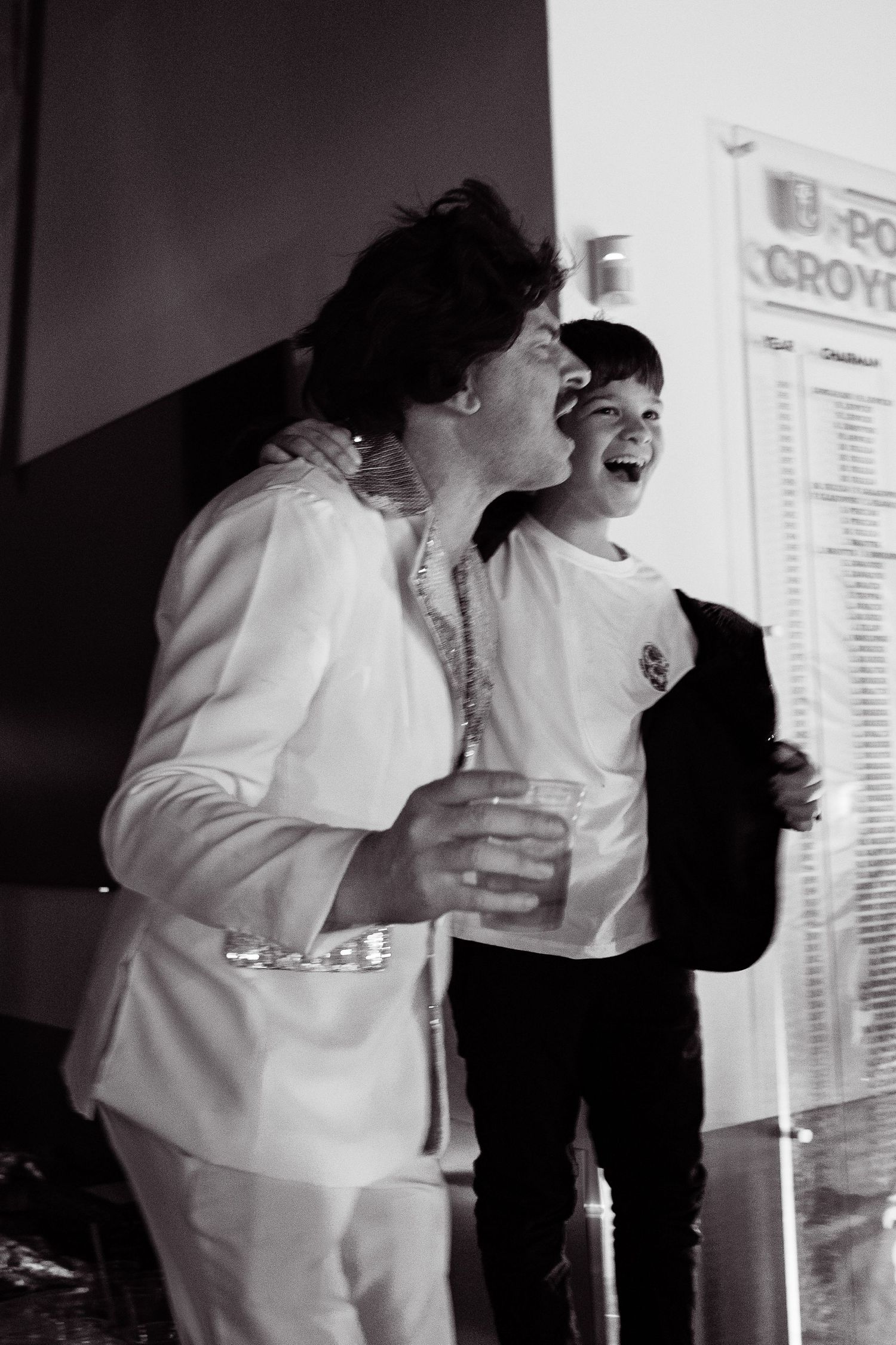 Black and white photo of a woman and laughing child in white outfits at a formal event.