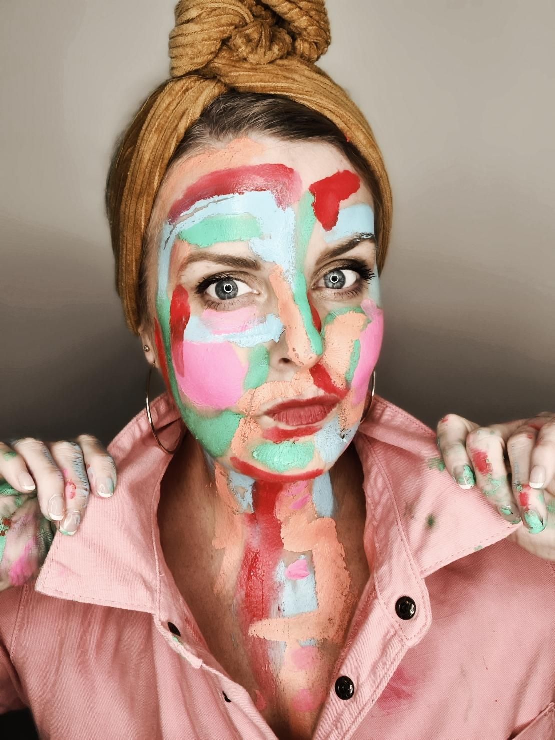 Woman with colorful abstract paint covering her face and hands wearing a pink shirt.