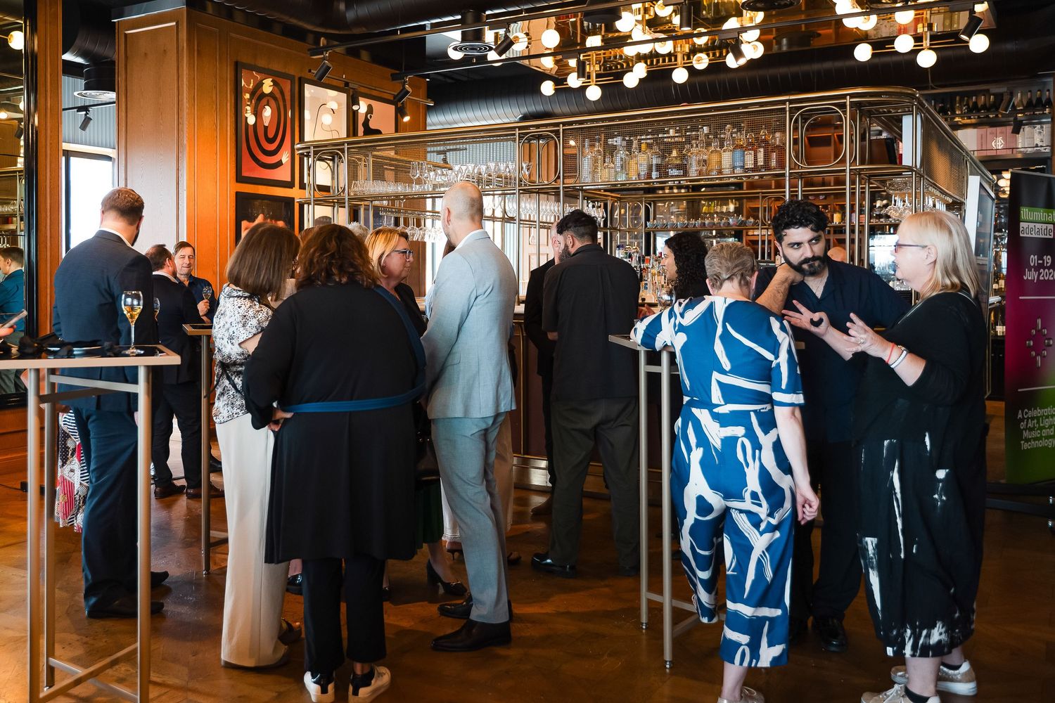 Guests mingling at an elegant indoor cocktail reception with a bar backdrop and warm ambient lighting.