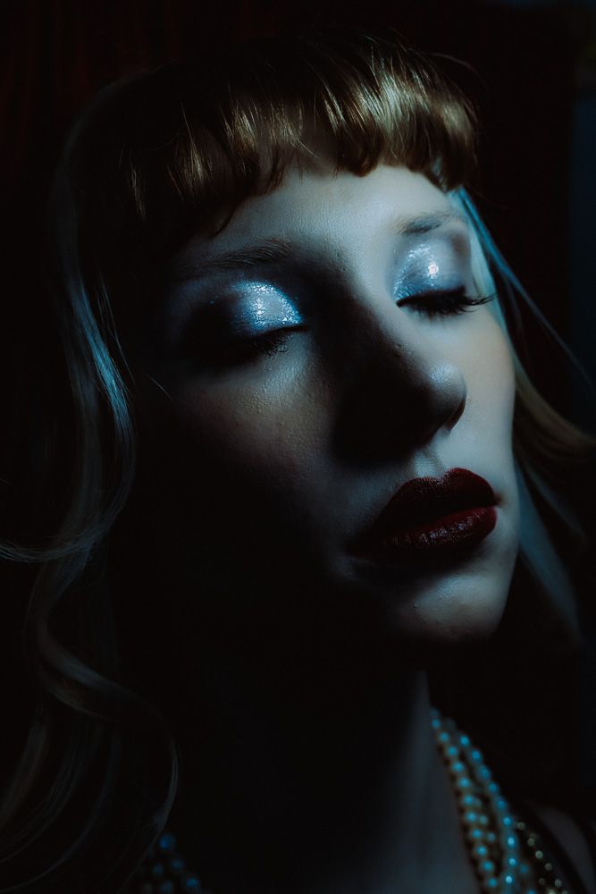 Woman with glittery eyeshadow and red lips posing in dramatic dark moody lighting.
