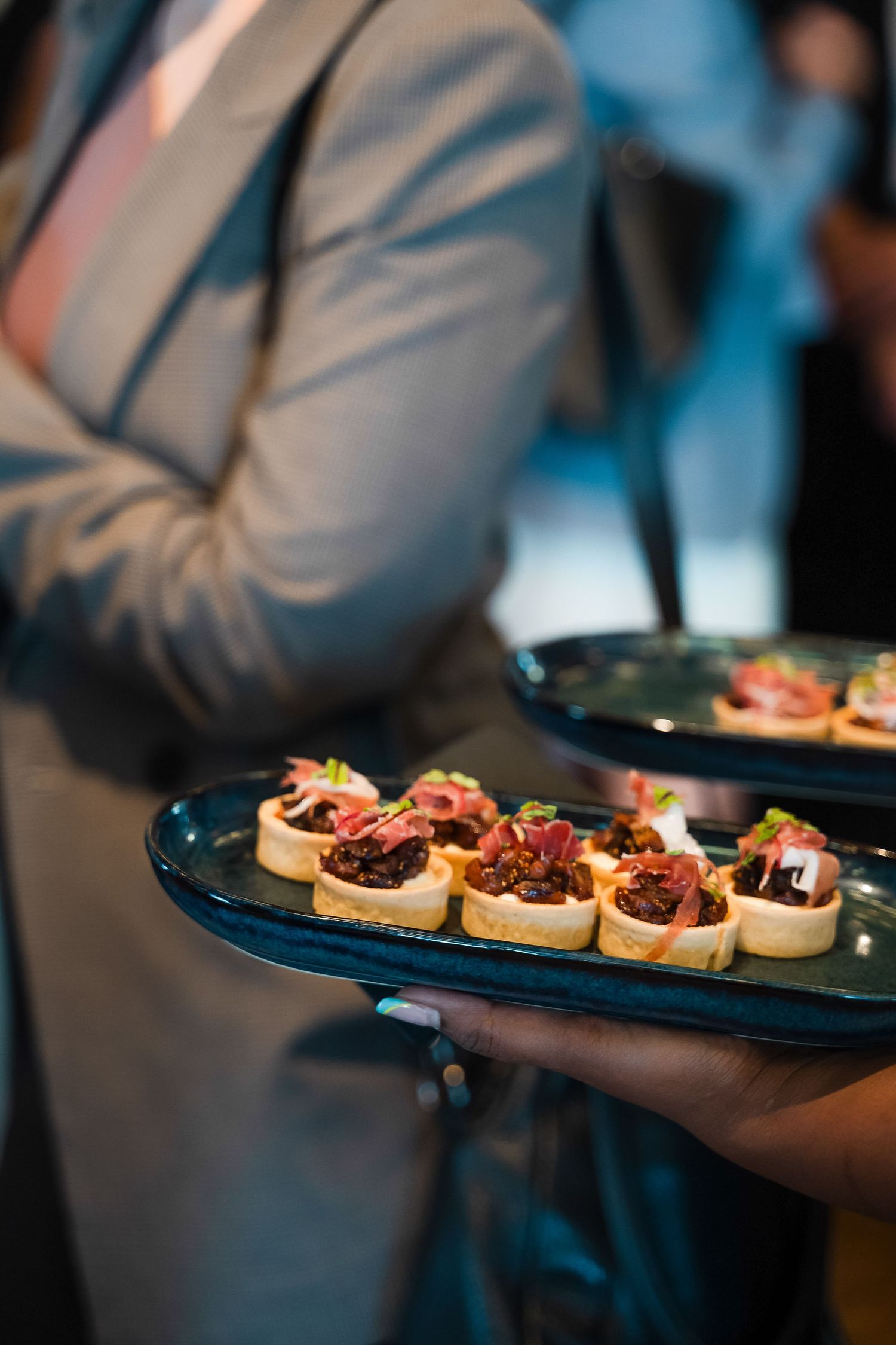 Waiter serving elegant canapés on dark blue ceramic platters at a formal catering event.