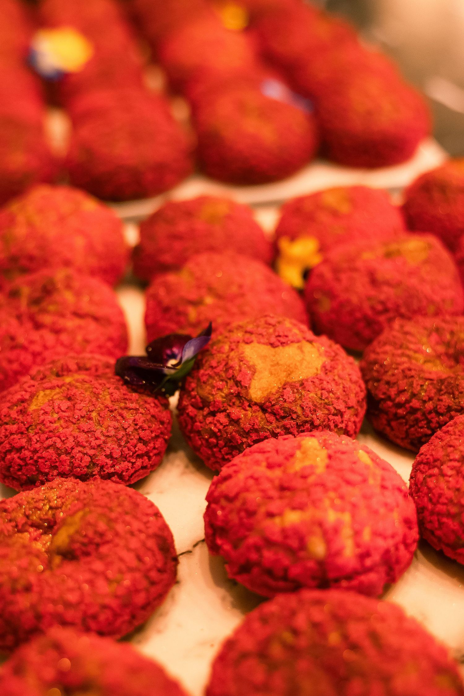 Rows of vibrant red velvet cookies displayed on a tray, garnished with small edible flowers.