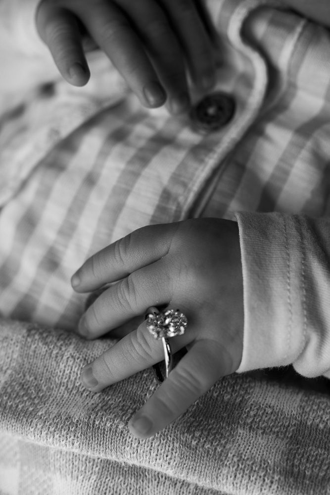 Black and white close-up of a baby hand wearing an oversized diamond ring on a soft blanket.