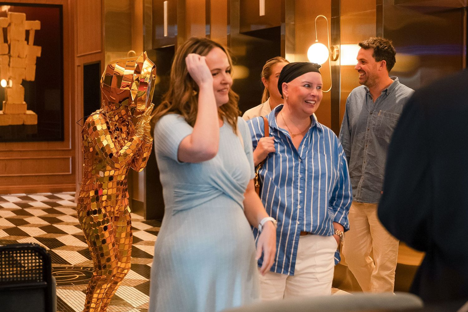 People laughing near a golden Oscar statue at an elegant indoor event with checkered floors.