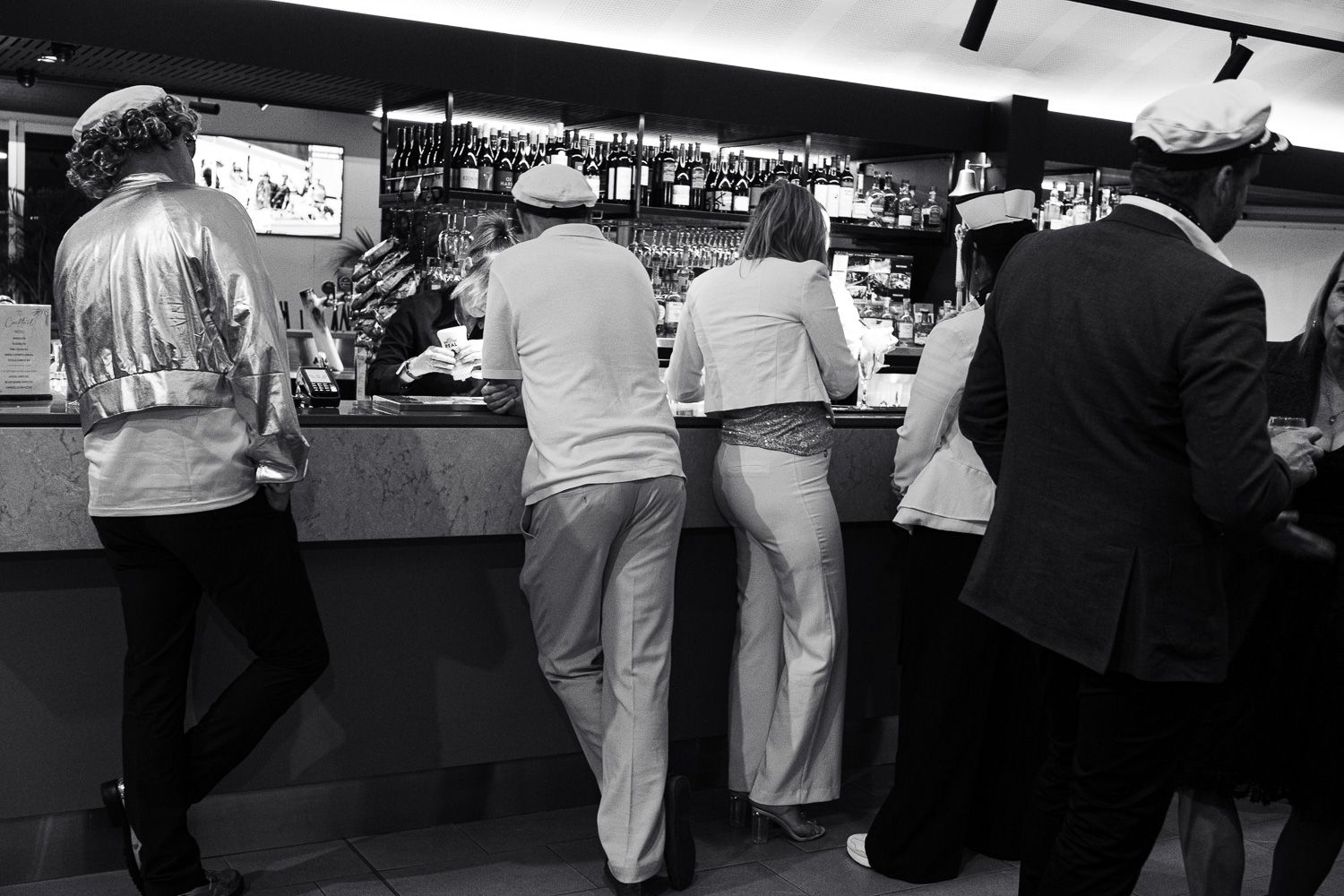 Black and white photo of people standing at a bar counter from behind in a restaurant.
