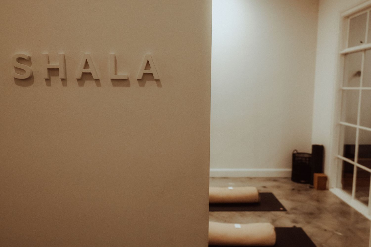 Minimalist yoga shala studio entrance with rolled mats and wooden blocks on a polished concrete floor.