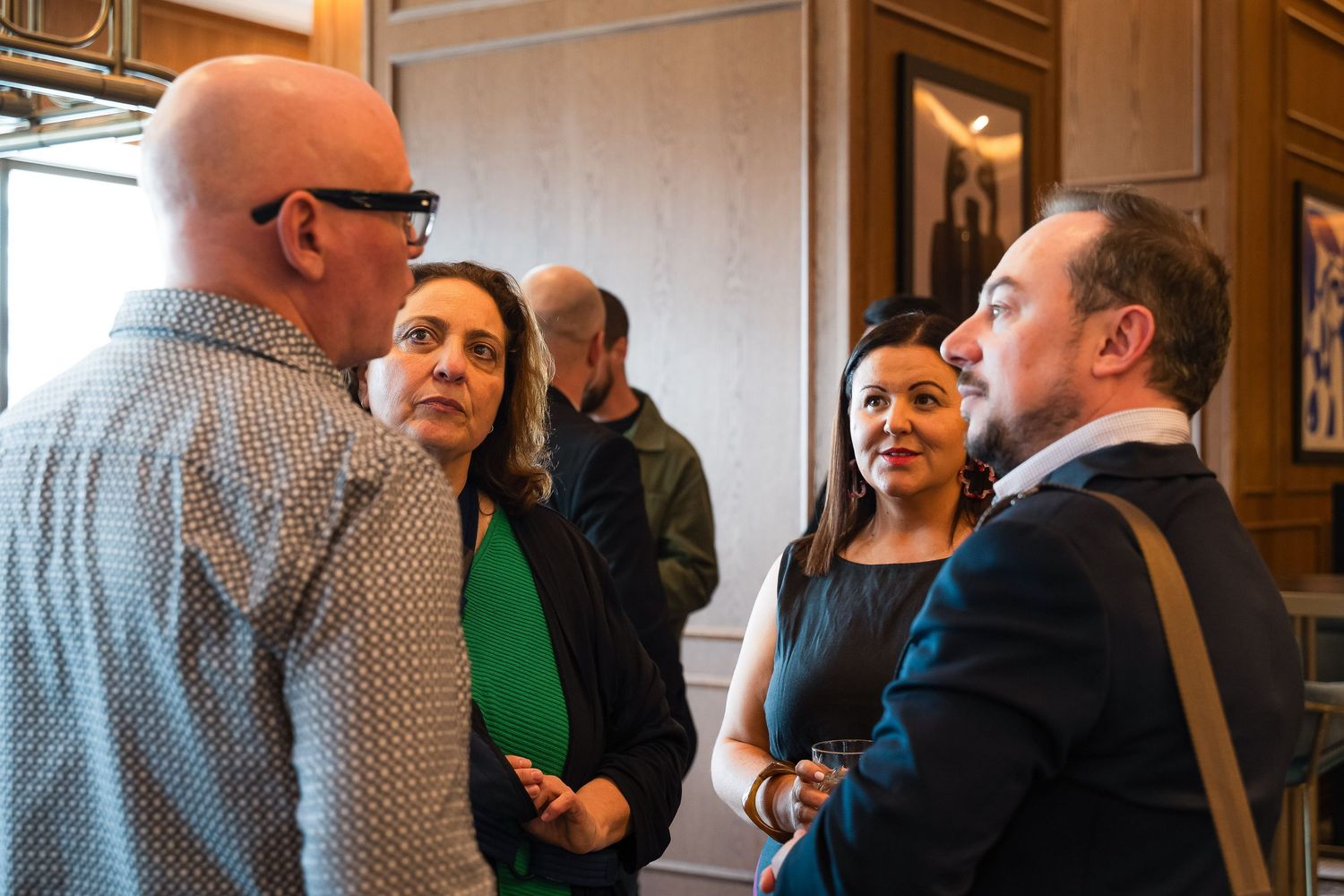 Group of professionals engaged in conversation at an indoor networking event in an elegantly decorated room.