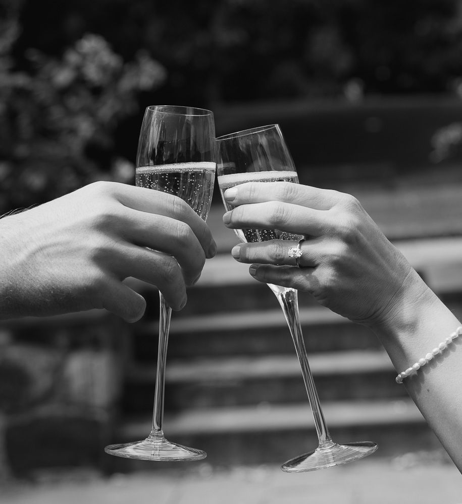 Two hands clinking champagne glasses in a celebratory toast, black and white photo.