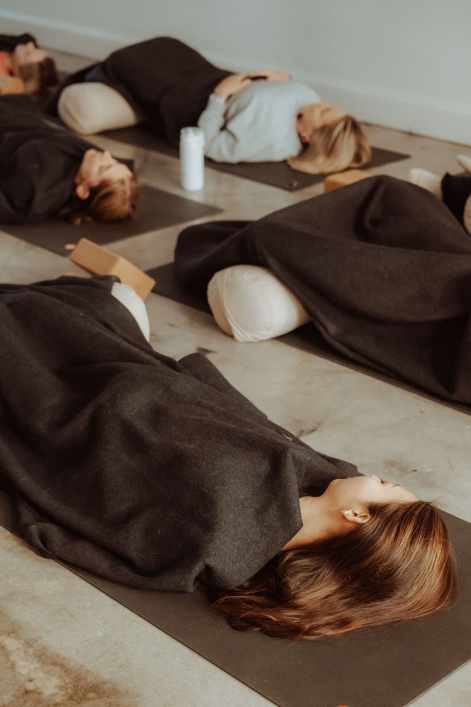 Group of people lying on yoga mats covered in dark blankets during a restorative yoga or meditation class.