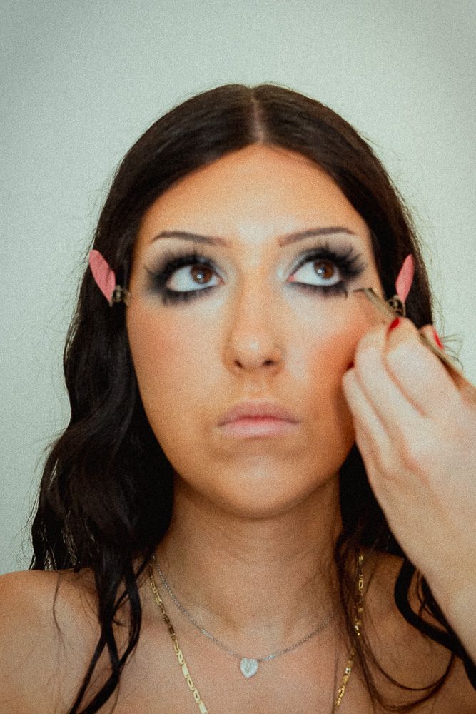 Woman with dramatic smoky eye makeup having false eyelashes applied by a makeup artist.