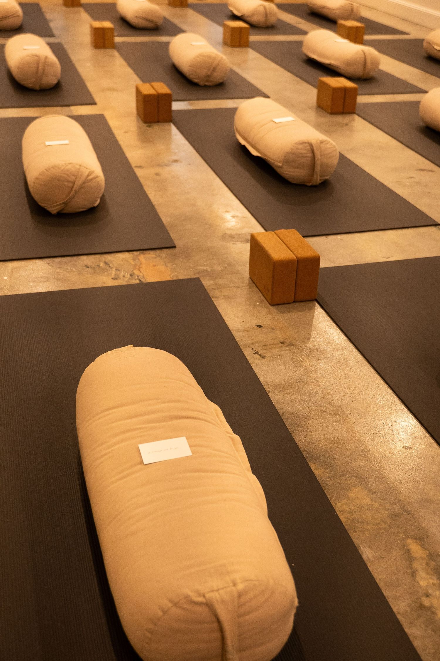 Yoga studio floor with beige bolster cushions and cork blocks arranged on dark gray mats.