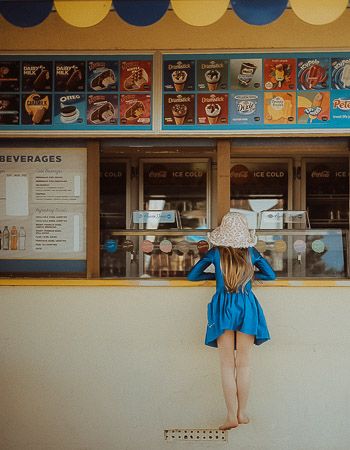 Young girl in blue dress ordering at a beachside ice cream and beverage concession stand.