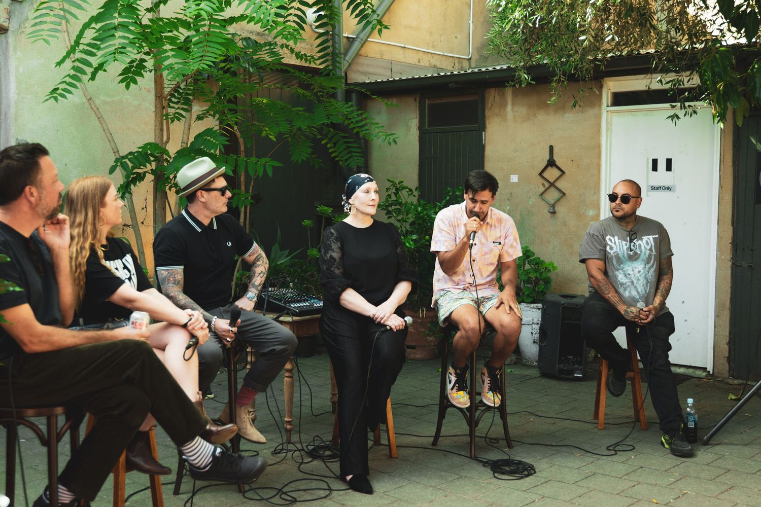 Group of people seated in a circle having an outdoor panel discussion in a courtyard.