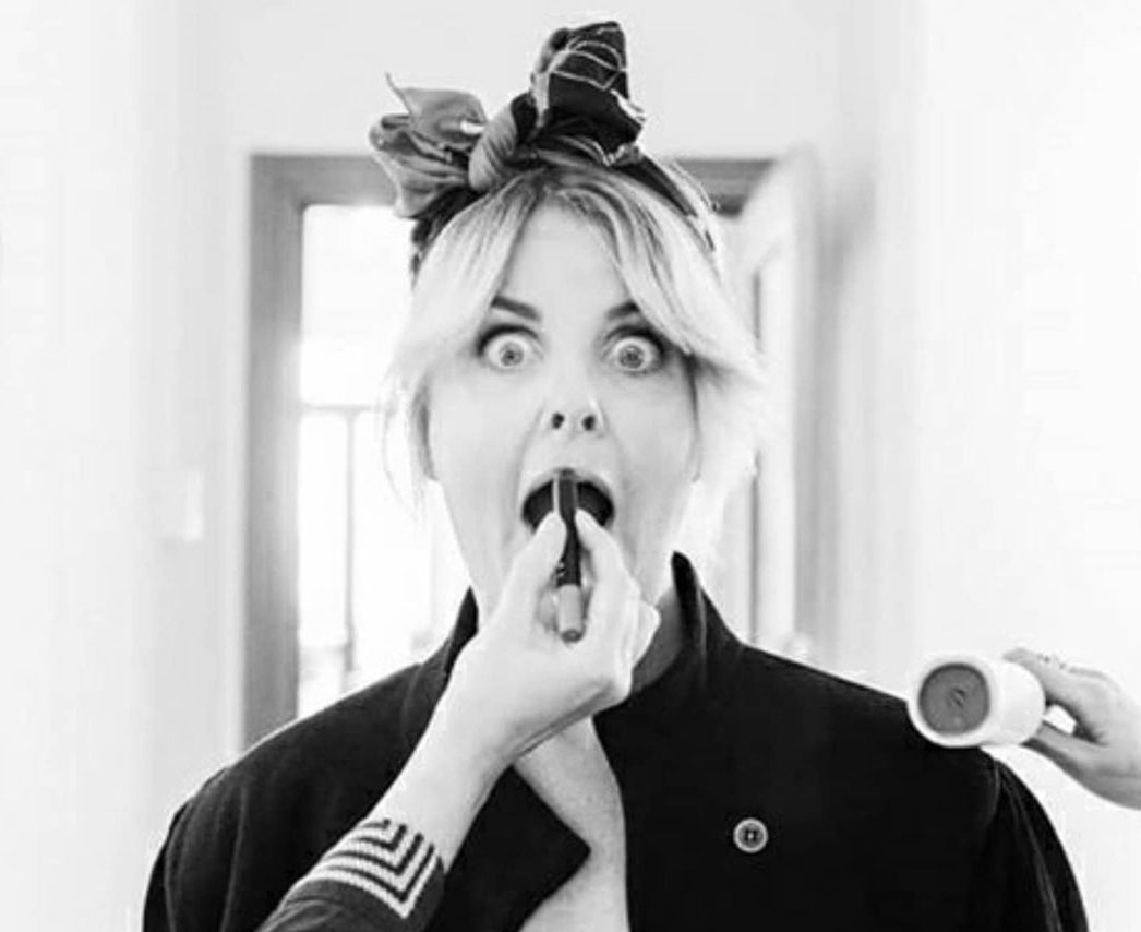 Black and white photo of a woman getting lipstick applied with a surprised expression.