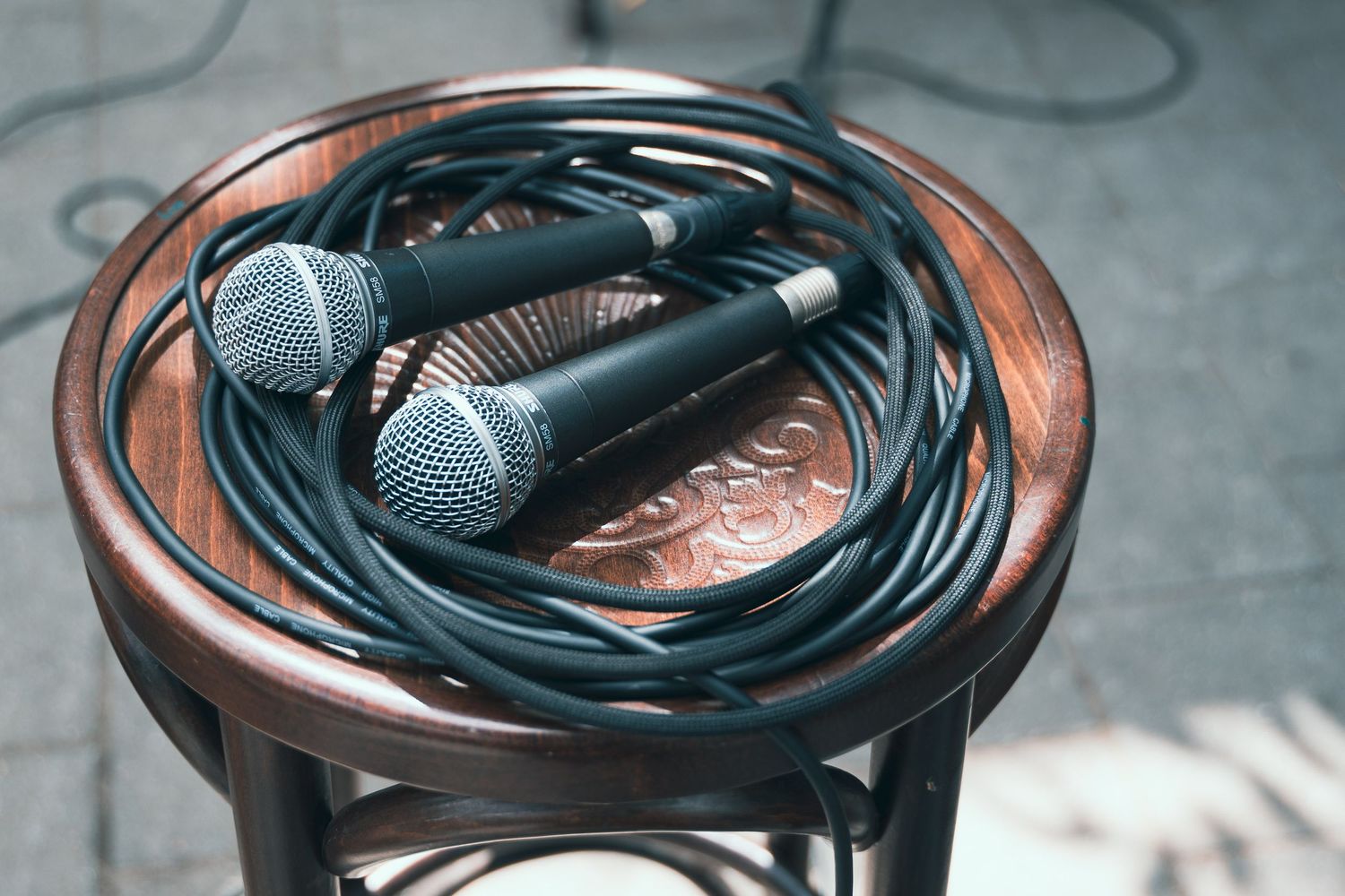 Two microphones with tangled black cables resting on a wooden stool outdoors.