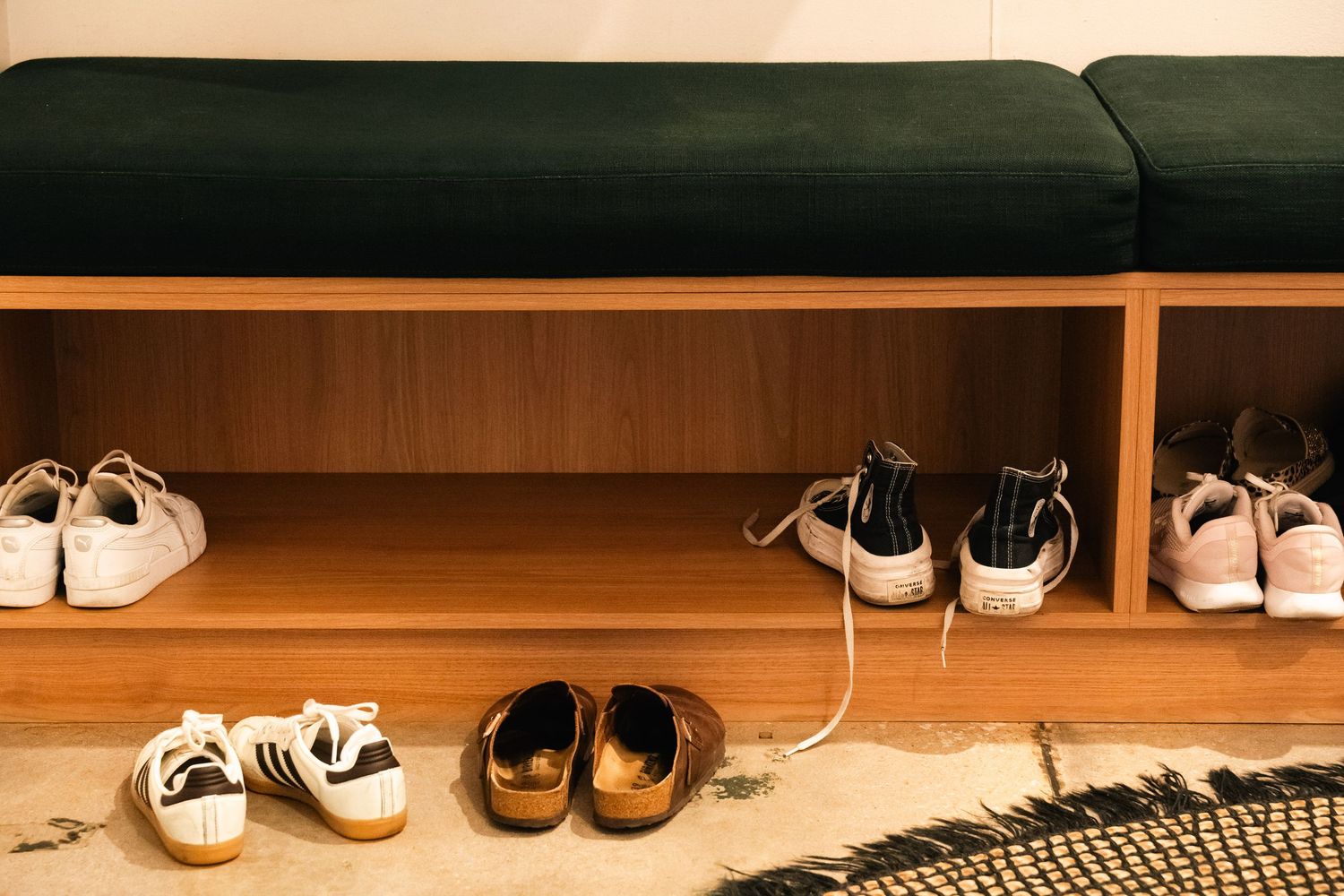 Wooden shoe bench with green cushion top, storing multiple sneakers and casual shoes in cubby shelves.
