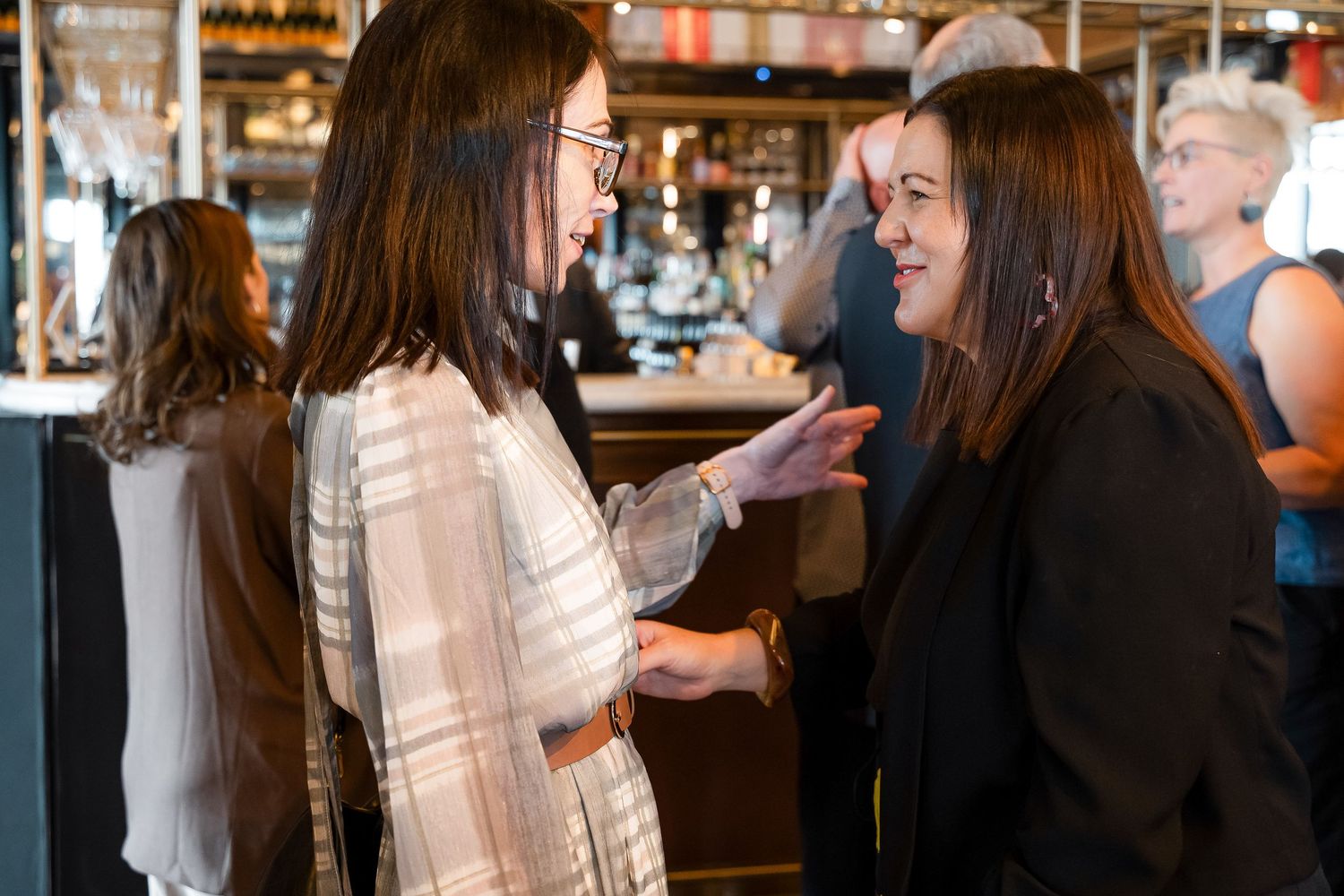 Two women engaged in conversation at a stylish bar or restaurant networking event.