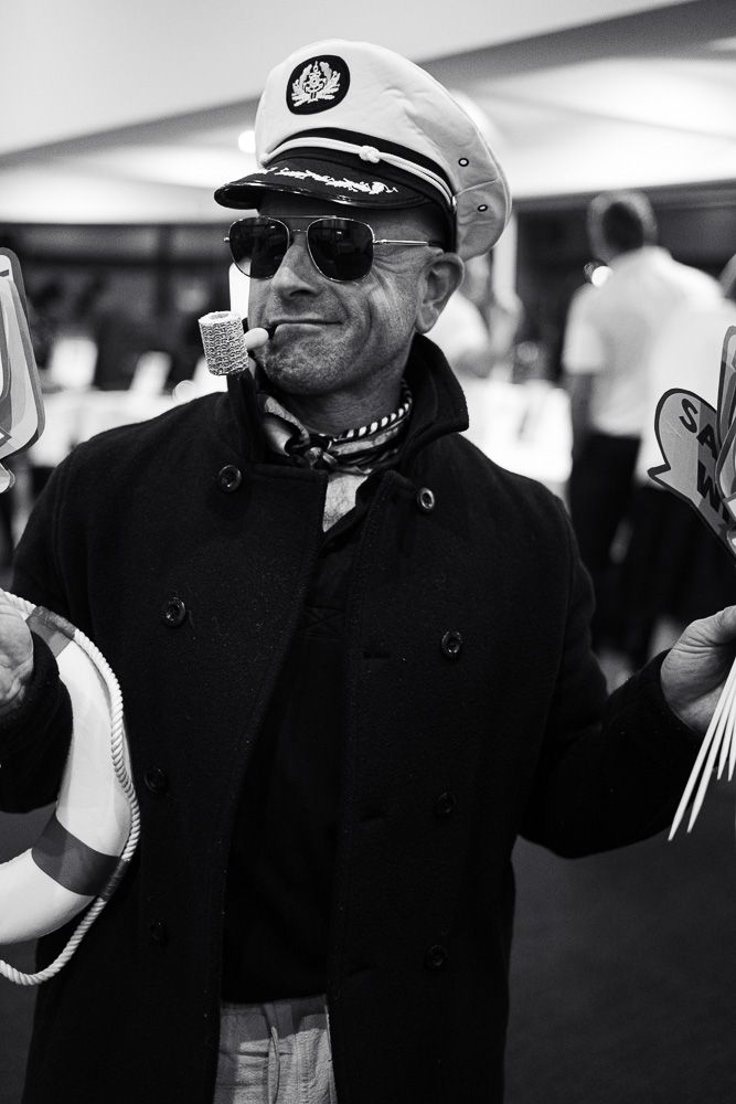 Black and white portrait of man dressed as sea captain with pipe, sunglasses, and life preserver.