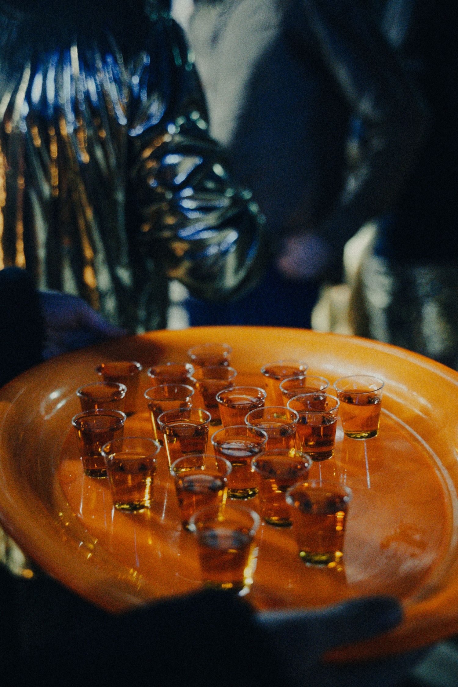 A tray of amber shot glasses filled with whiskey or tequila served at a party event.