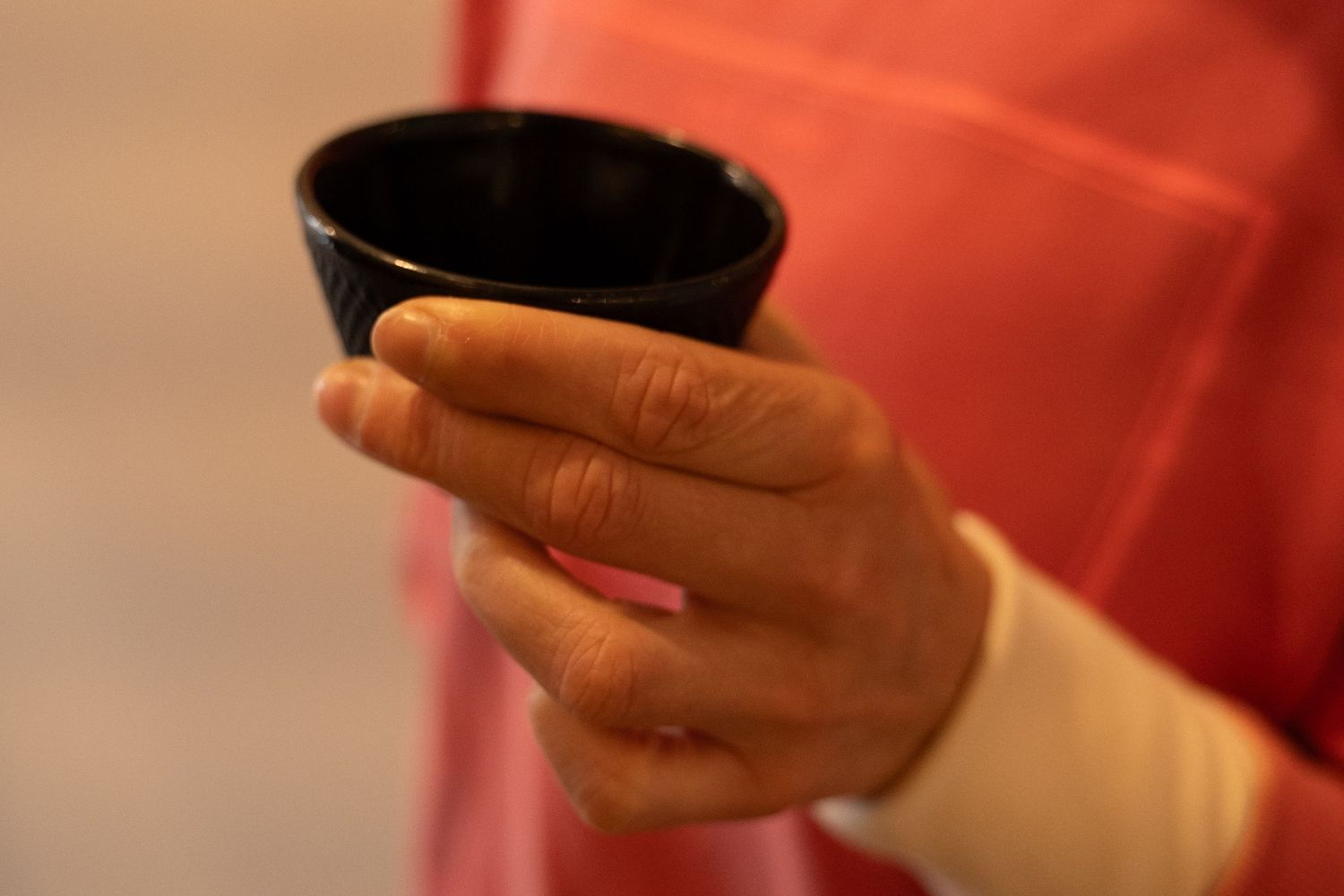 Person in red robe holding a small black ceramic tea bowl during a traditional Japanese tea ceremony.