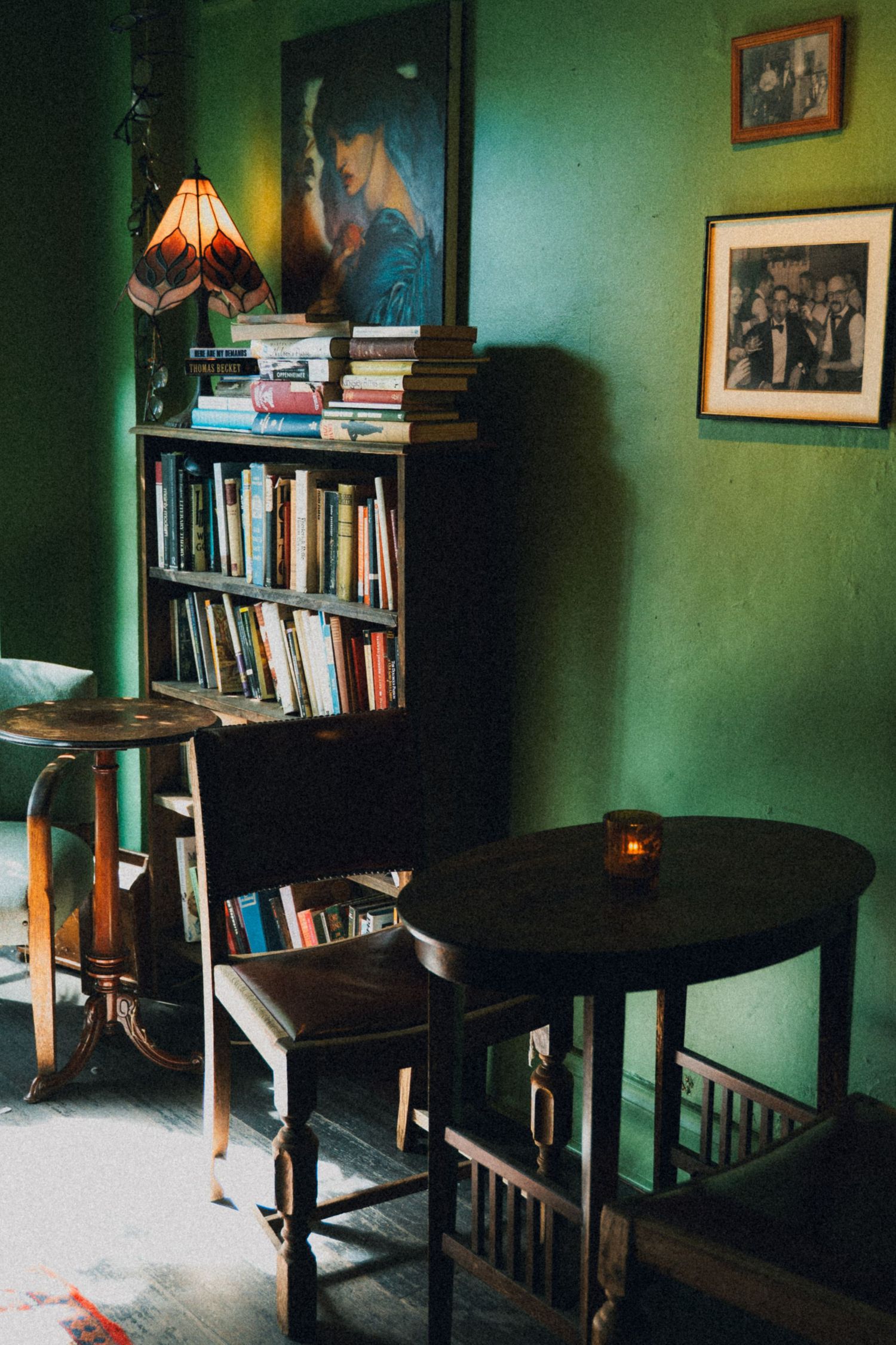 Cozy vintage reading nook with green walls, wooden bookshelf filled with books, small round table, and warm lamp light.