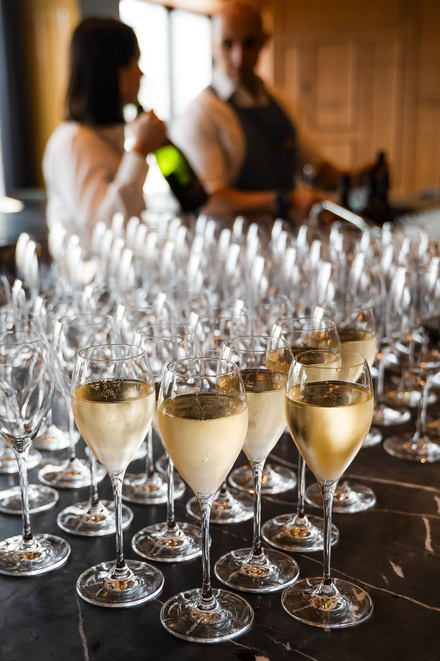 Rows of champagne flutes filled with sparkling wine arranged on a dark table at an elegant catered event.