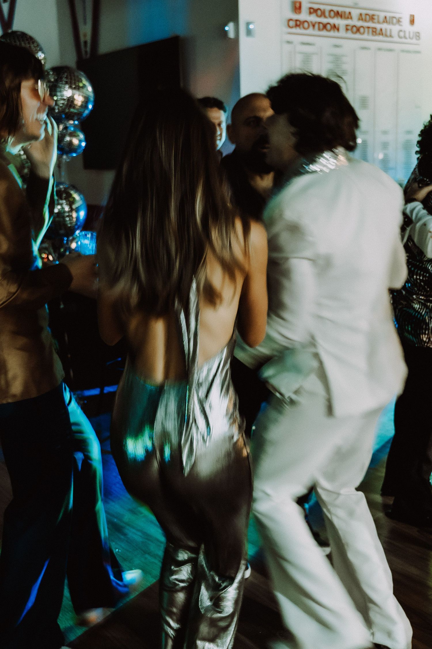 People dancing at a disco-themed party with silver balloons and blue lighting at Polonia Adelaide Croydon Football Club.