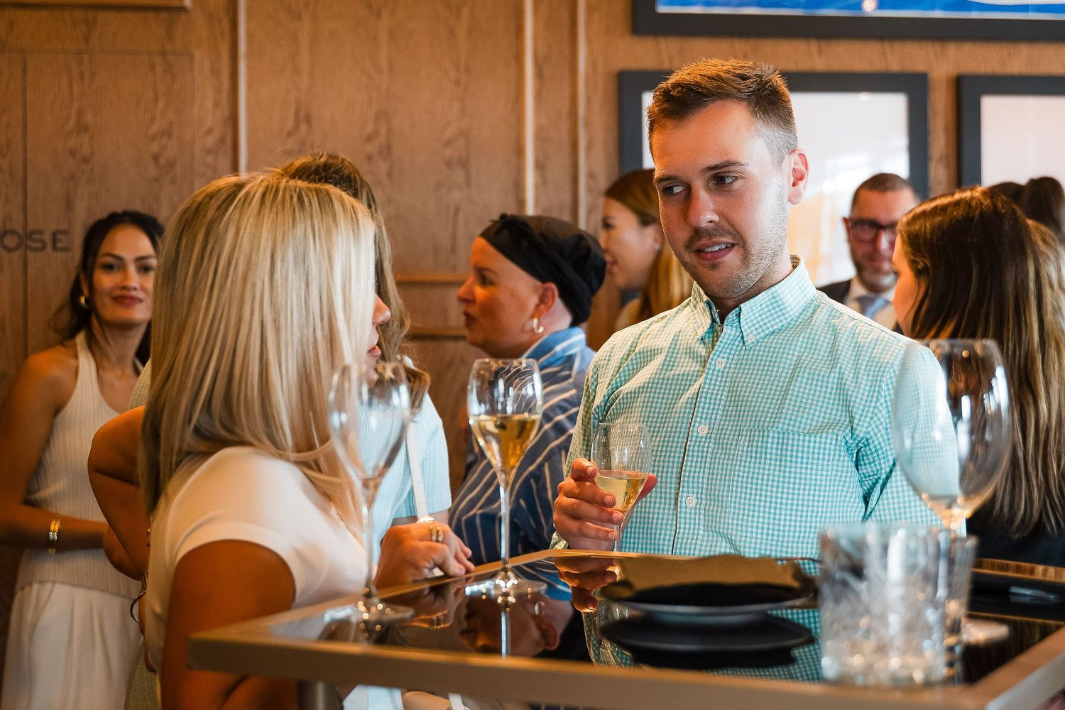 People socializing at an upscale bar, holding wine glasses and engaging in conversation in a warmly lit venue.