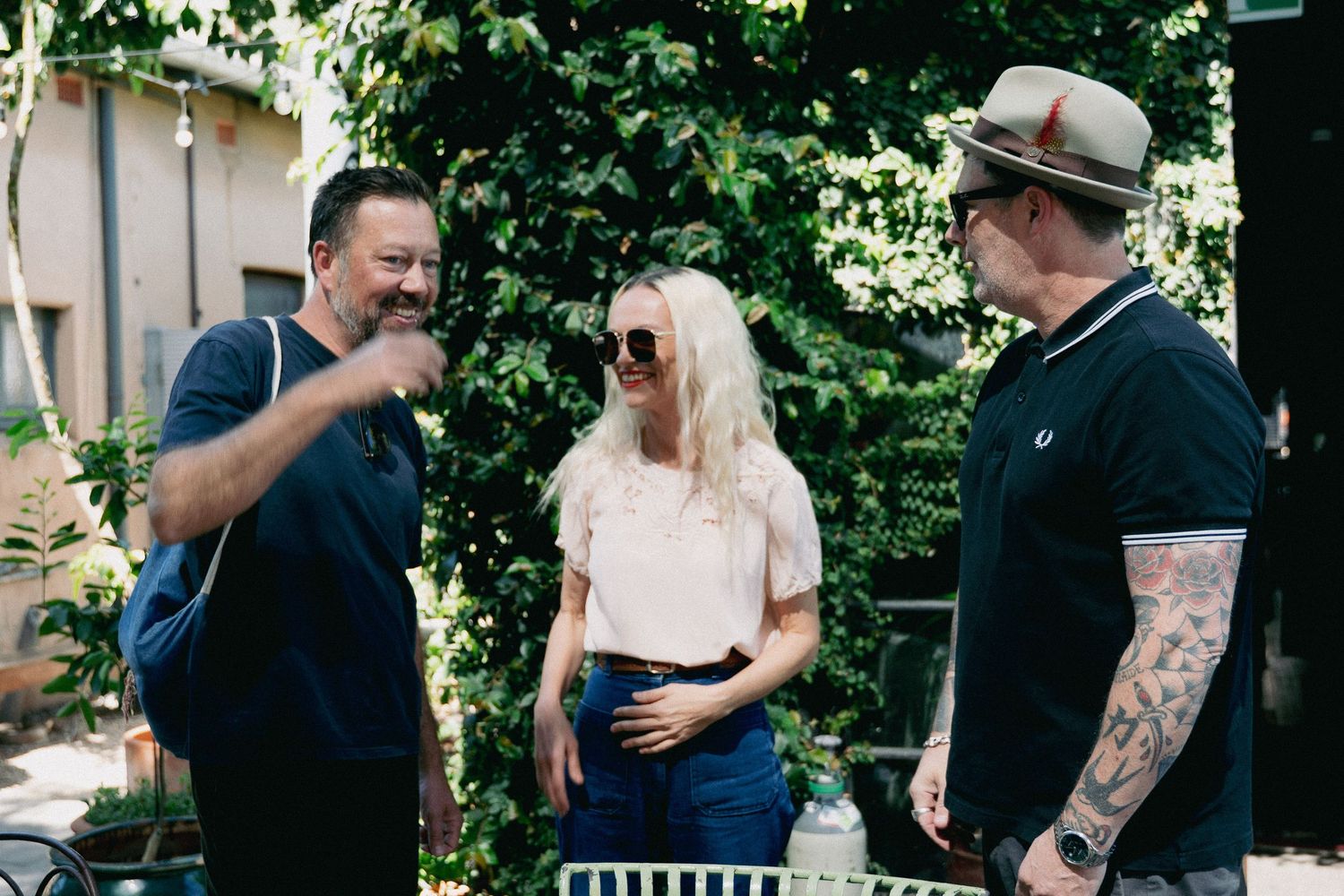 Three friends laughing and conversing outdoors in a lush garden setting on a sunny day.