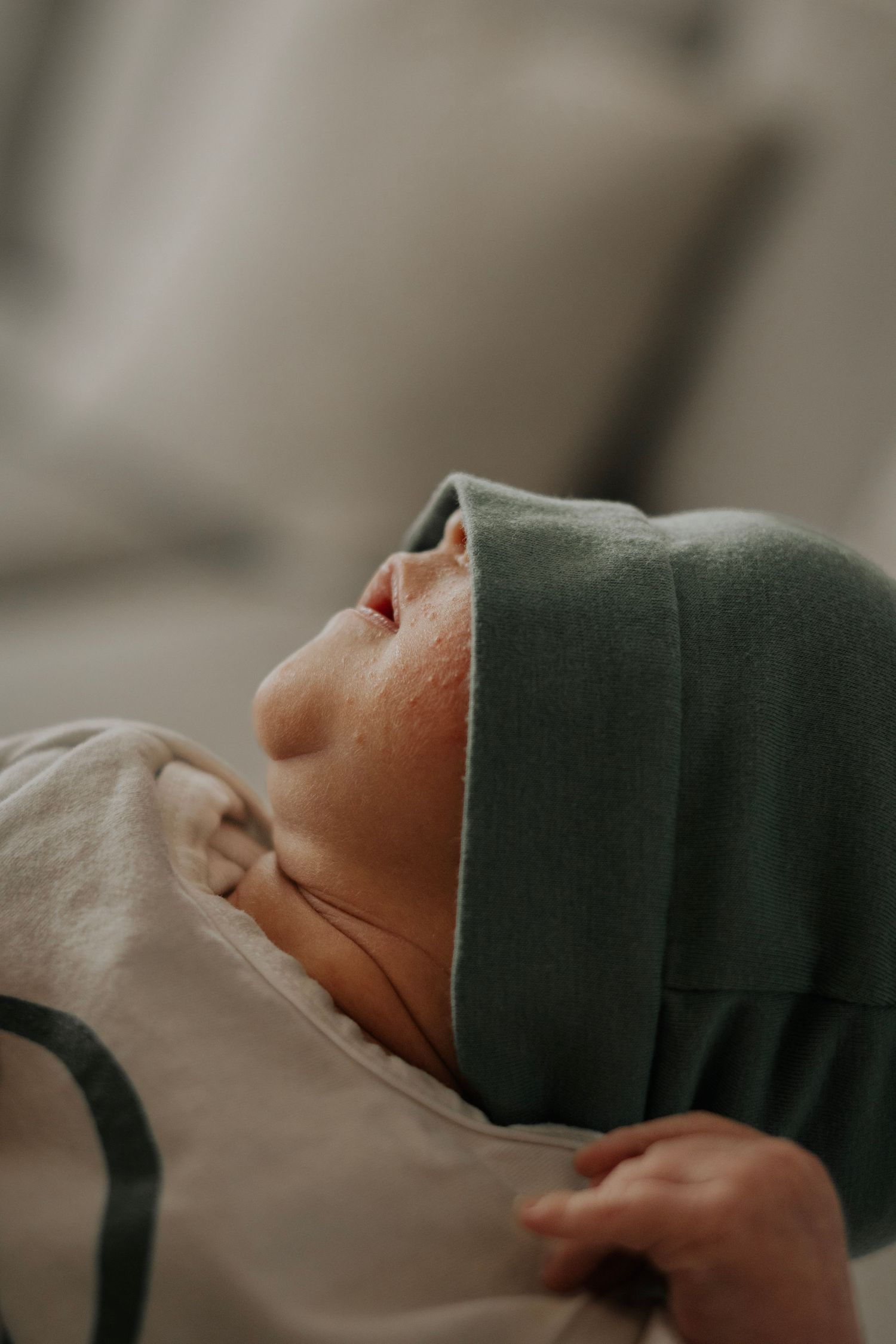 Newborn baby in green hat and white swaddle blanket resting peacefully.