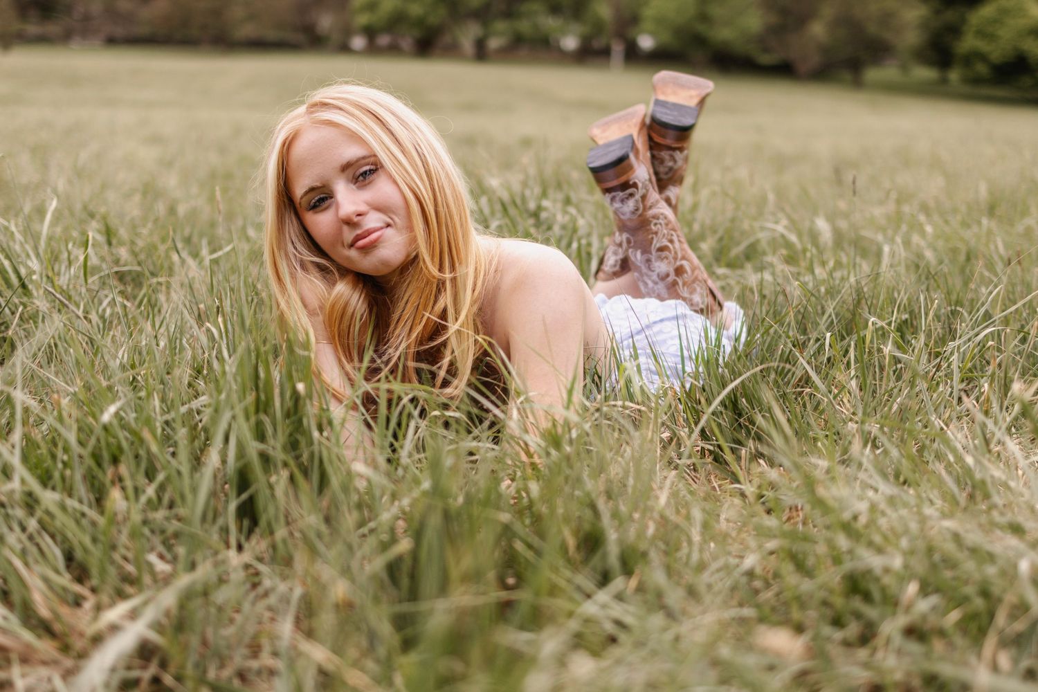 Blonde woman lying in tall green grass wearing a white dress and patterned socks outdoors.