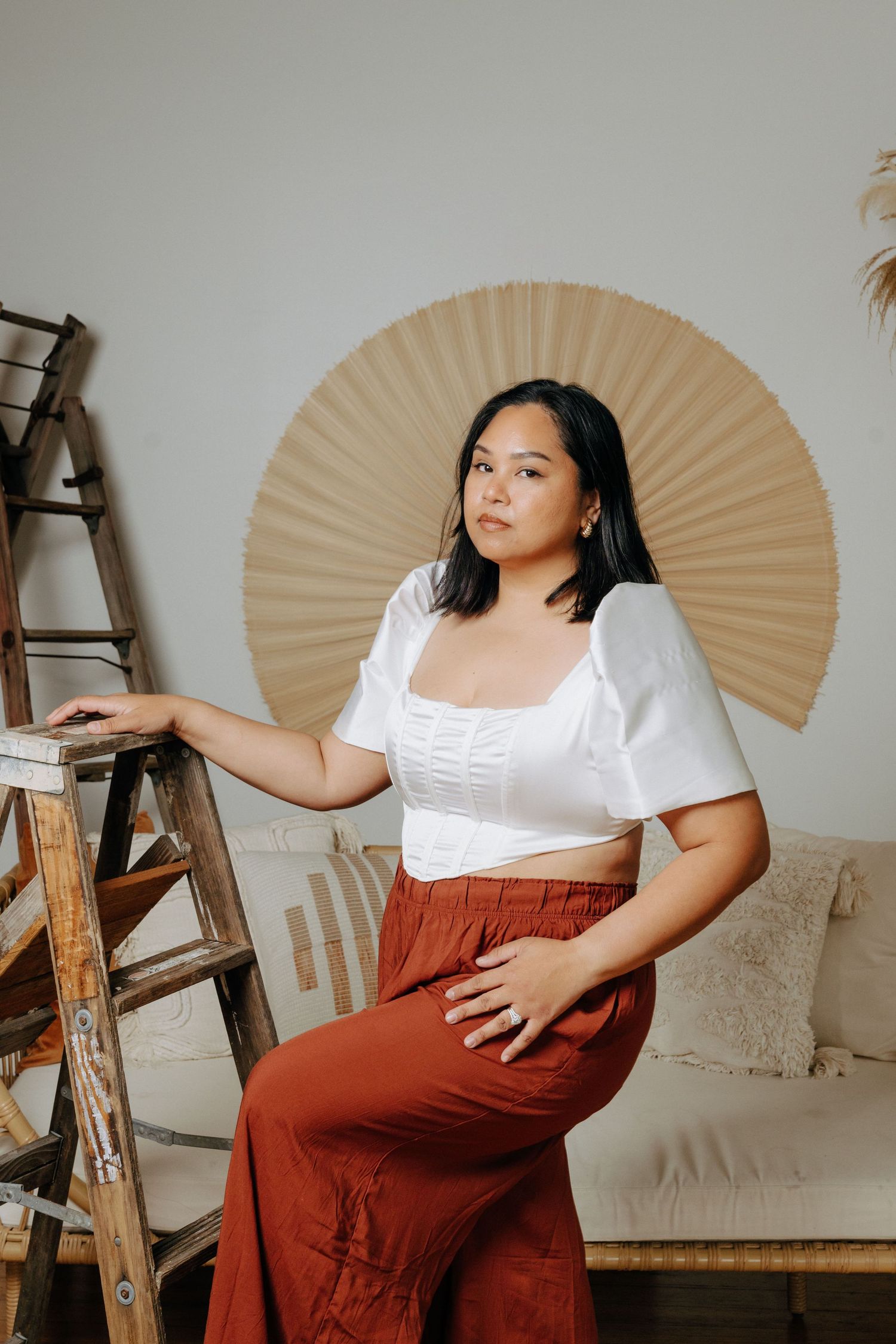 Portrait in front of a decorative fan with wooden ladder and cozy home decor elements.