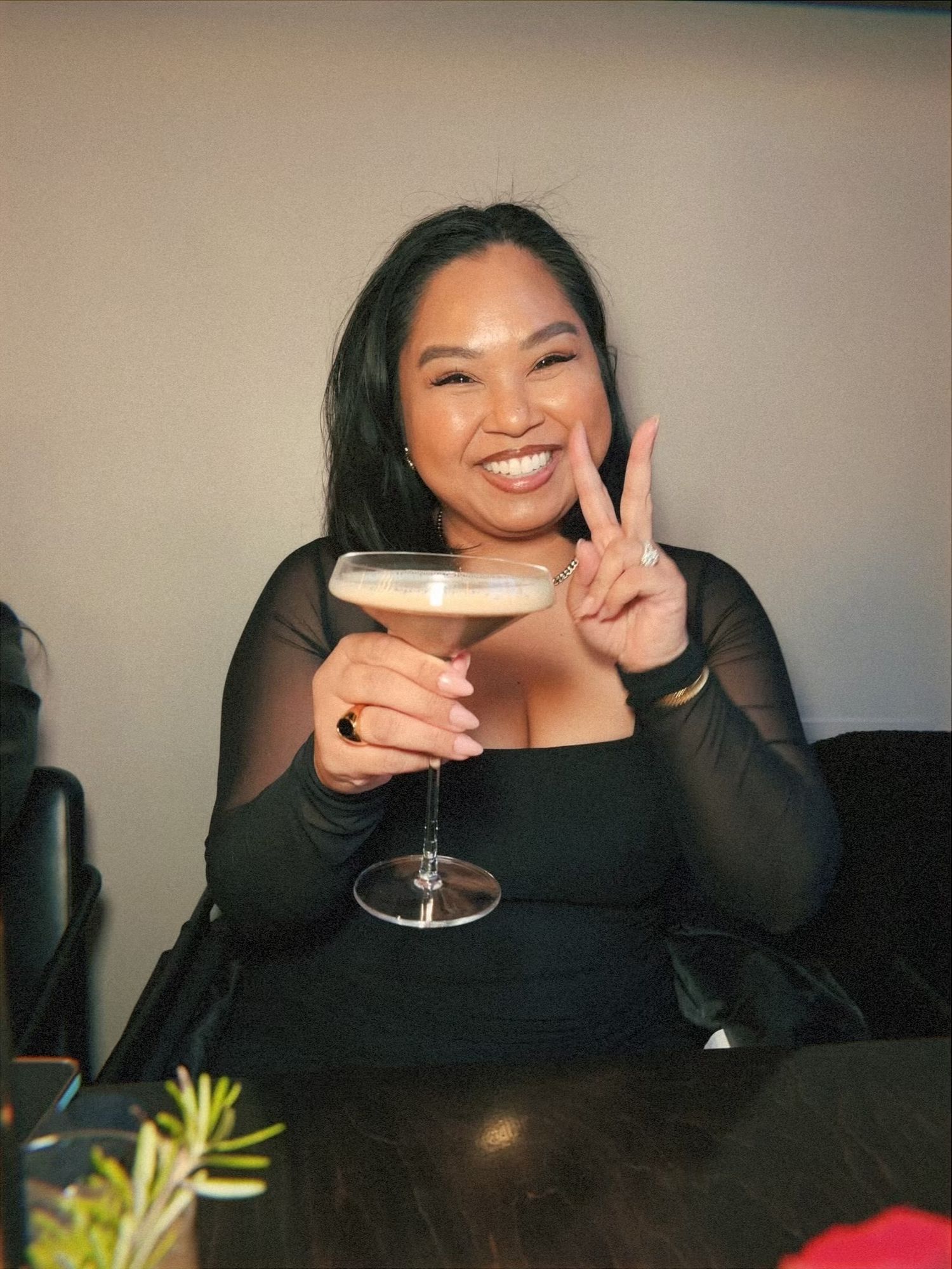 Person enjoying a martini cocktail while making peace sign at restaurant.