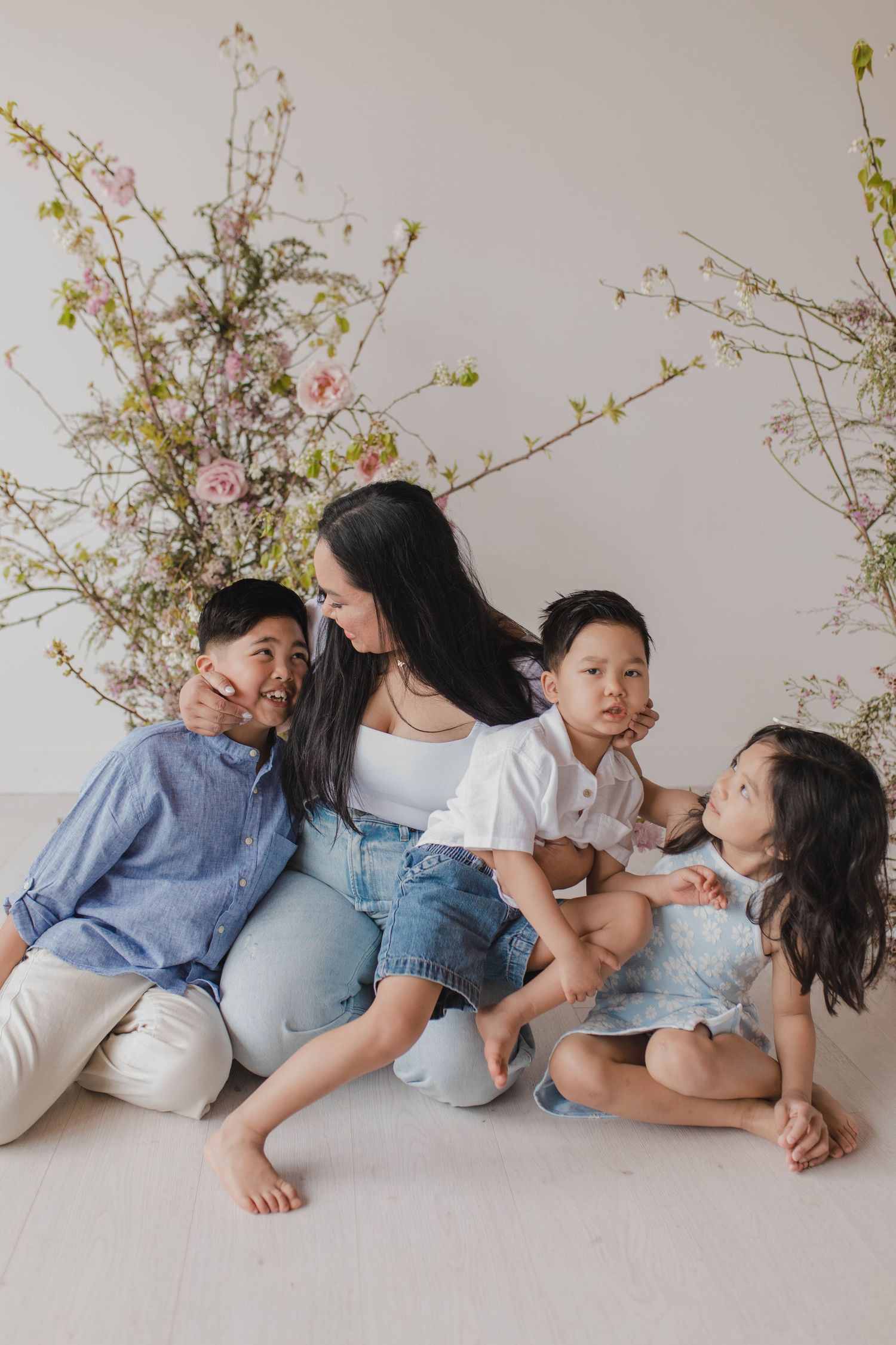 Family portrait with floral backdrop showing playful interaction and casual denim outfits.