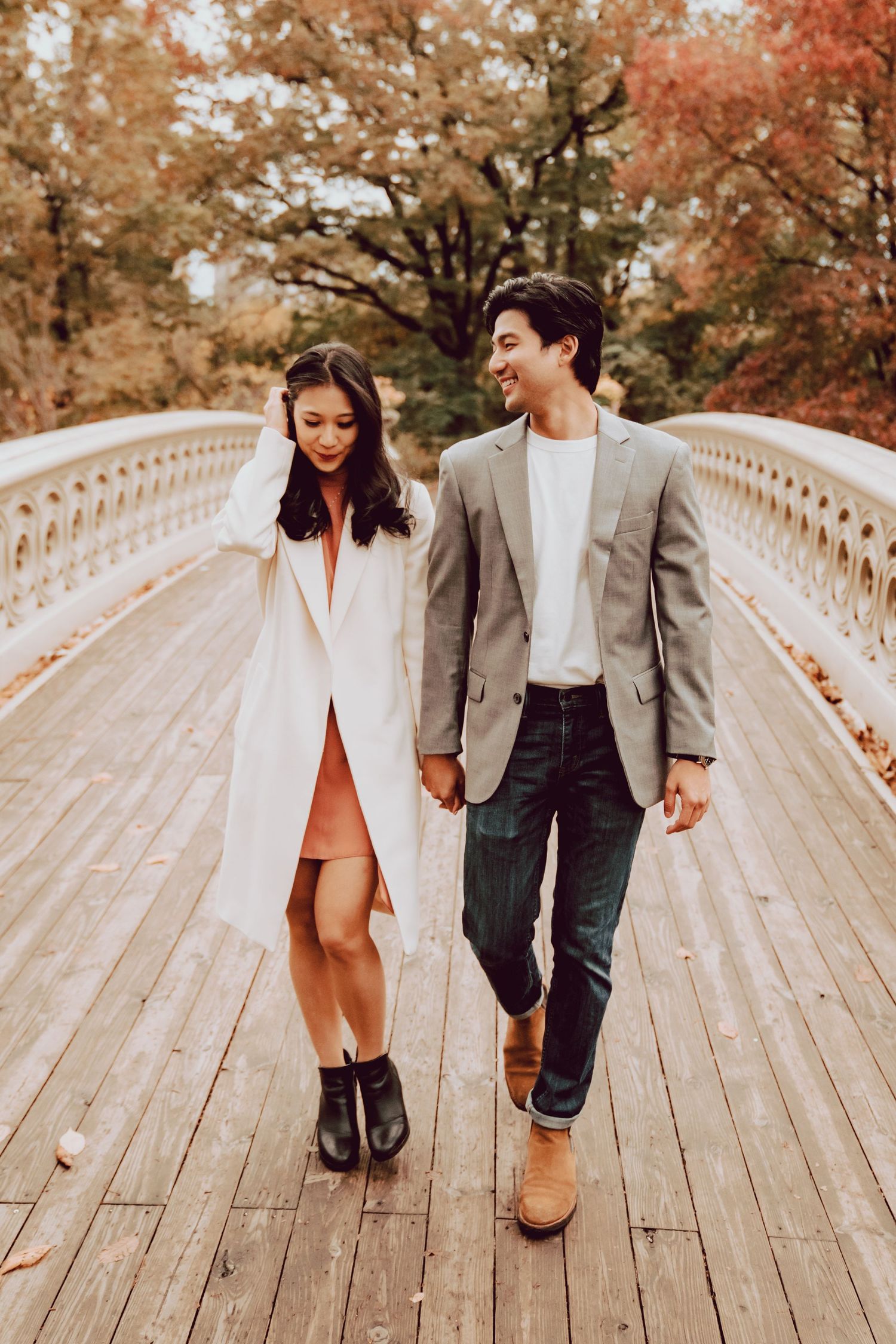 couple happily walking across the bow bridge in Central Park during their engagement session