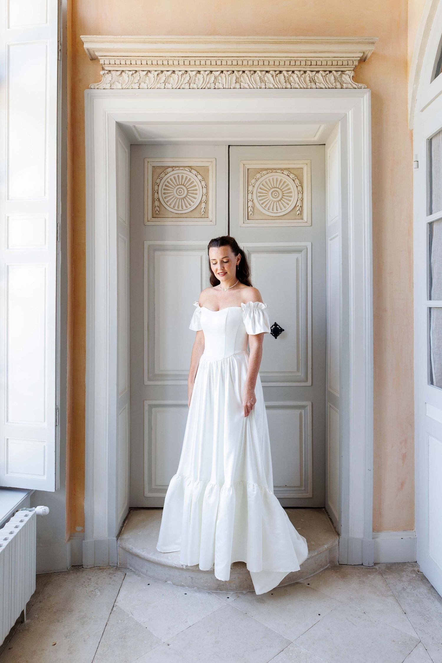 Une photos artistiques montrant une mariée en robe blanche devant des portes au Château de Bonnemare en Normandie