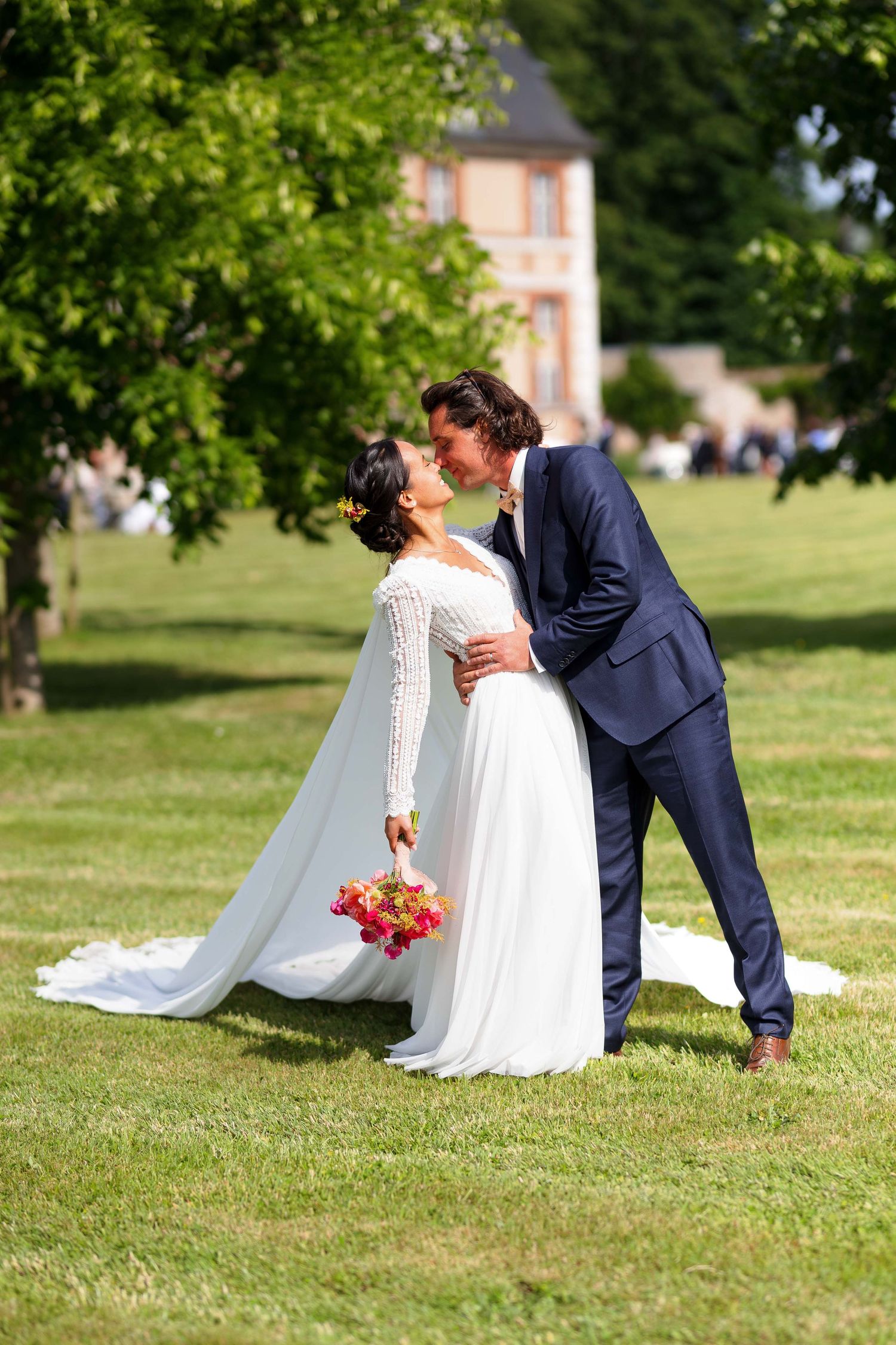 Un couple en tenue de mariage partage un tendre moment sur une pelouse ensoleillée, avec en arrière-plan la Château d'Argeronne