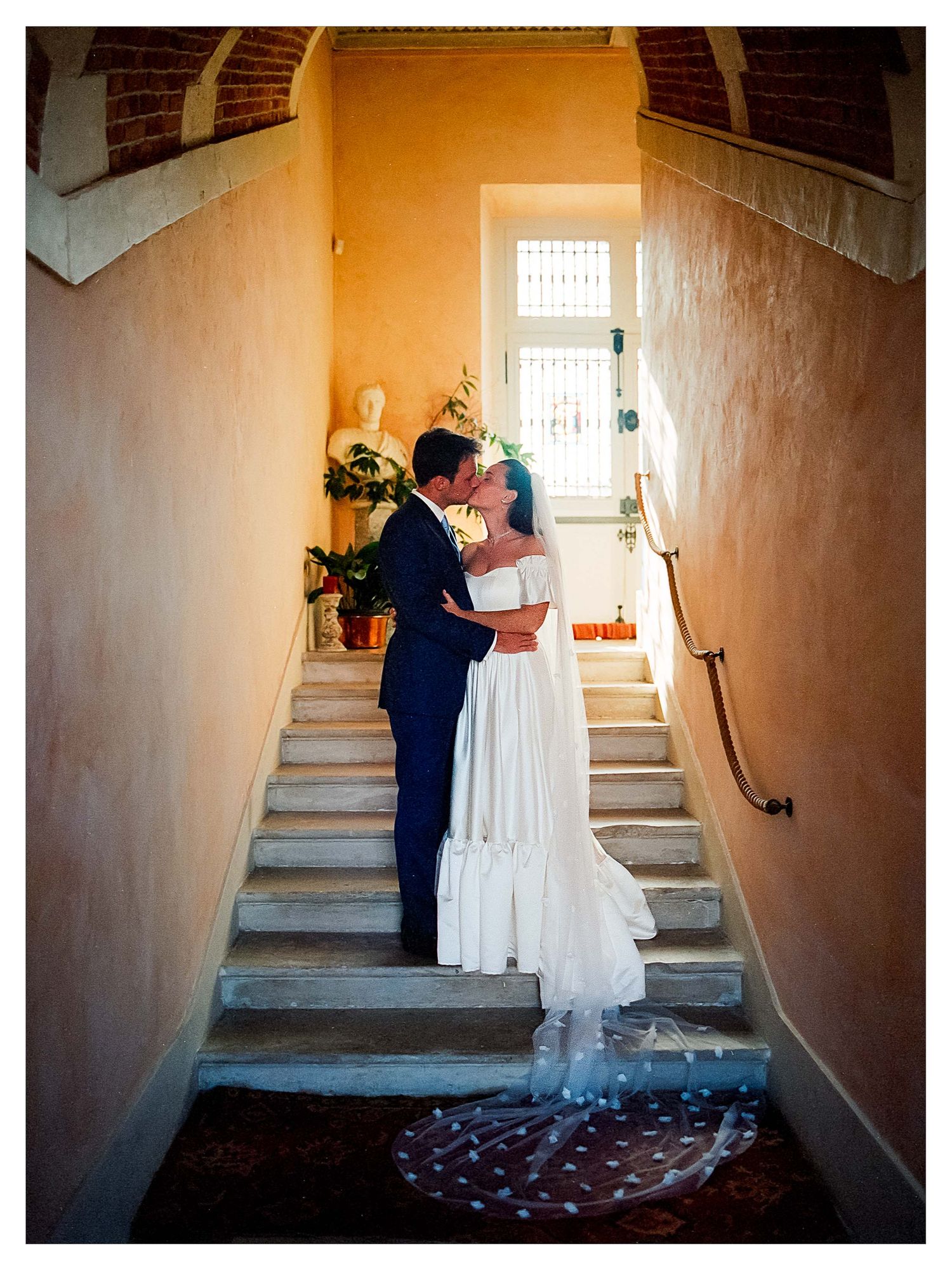 Un couple partage un moment d'intimité dans une cage d'escalier aux murs blancs, ornée de pétales de rose au Château de Bonnemare à Radepont